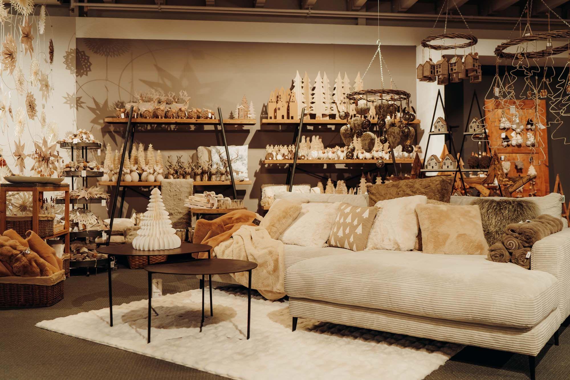 Gemütliche Wohnzimmer-Ausstellung mit beiger Couch, natürlicher Weihnachtsdeko und warmen Holzregalen bei Möbel Grell.