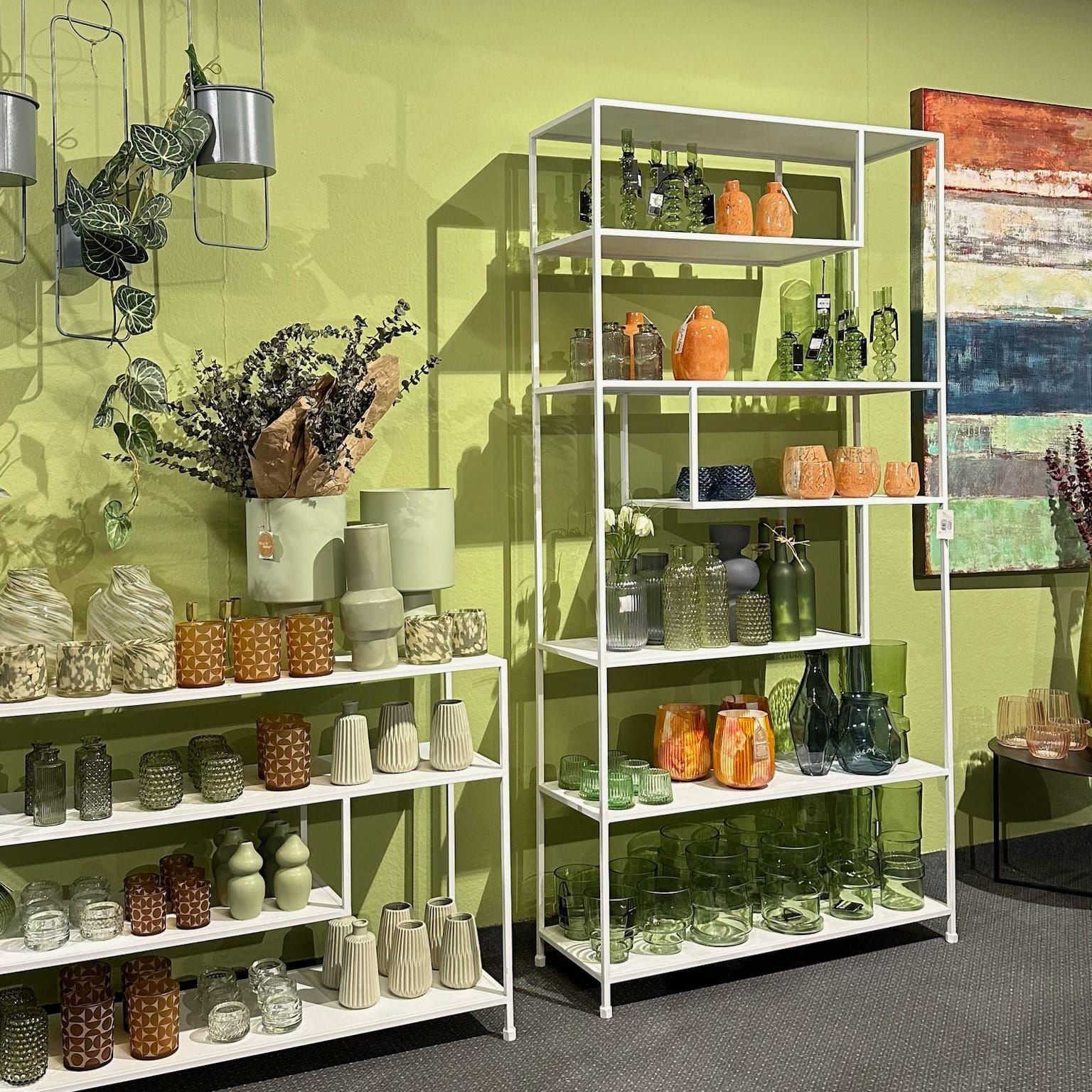 Große Frühjahrs-Ausstellung mit Vasen, Windlichtern und Pflanzen vor grüner Akzentwand und bunter abstrakter Kunst.