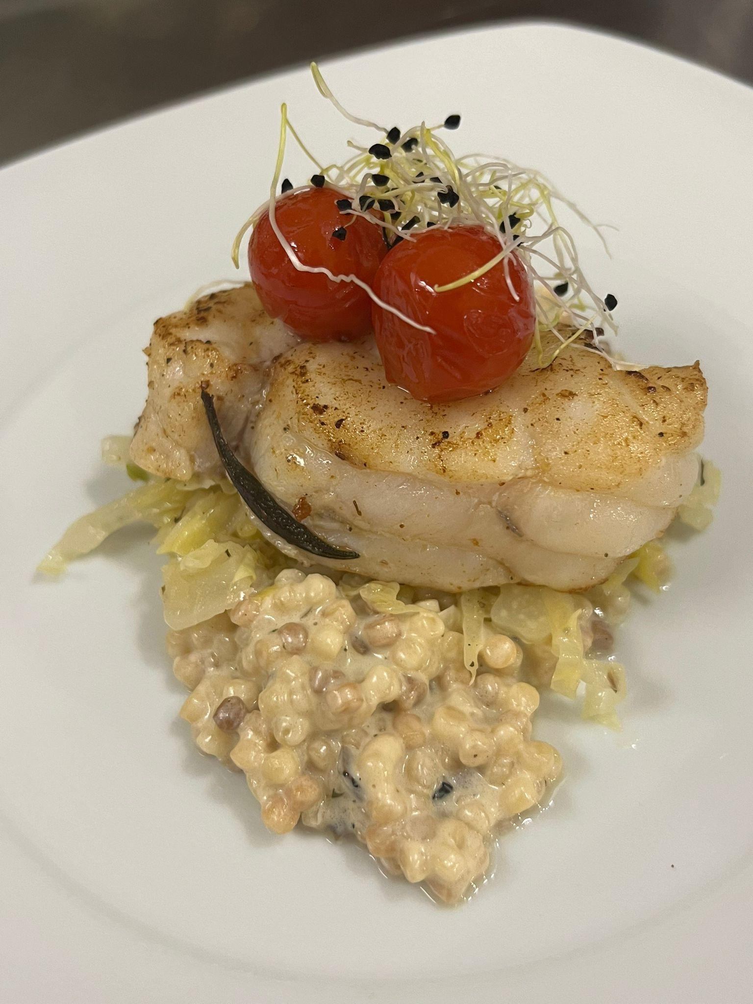 Eleganter Fischteller mit gebratenem Fischfilet, glasierten Kirschtomaten, Kresse-Garnierung und cremigem Risotto auf weißem Teller angerichtet.