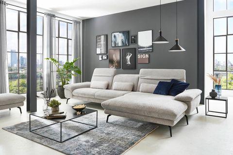 Modernes Ecksofa in hellem Stoff mit Relaxfunktion in stilvollem Wohnzimmer – kombiniert mit schwarzem Couchtisch, Wanddeko und großen Fensterfronten.