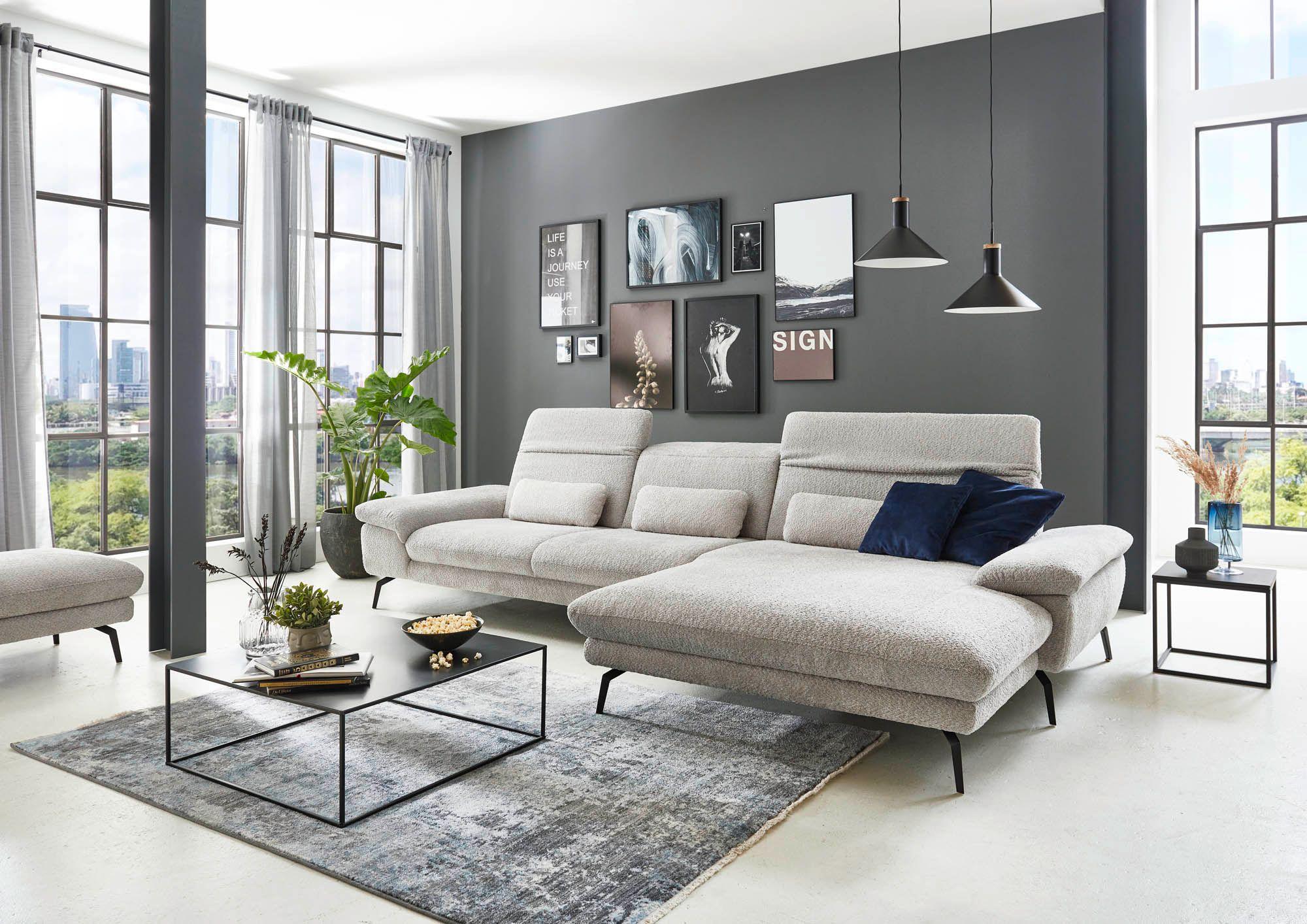 Modernes Ecksofa in hellem Stoff mit Relaxfunktion in stilvollem Wohnzimmer – kombiniert mit schwarzem Couchtisch, Wanddeko und großen Fensterfronten.