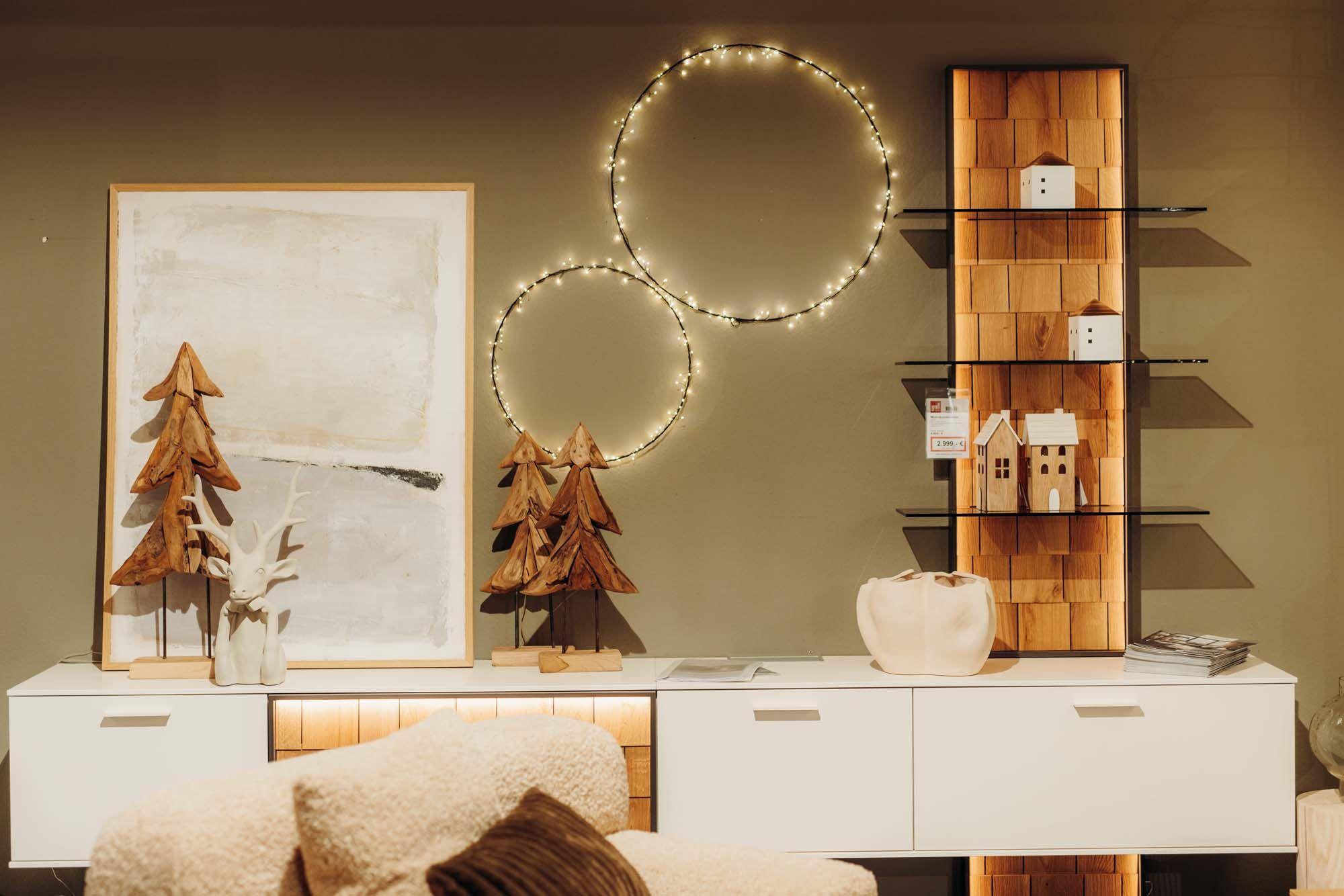 Modernes Sideboard mit Holztannenbäumen, LED-Ringen und minimalistischer Winterdeko in Weiß-Holz-Optik.