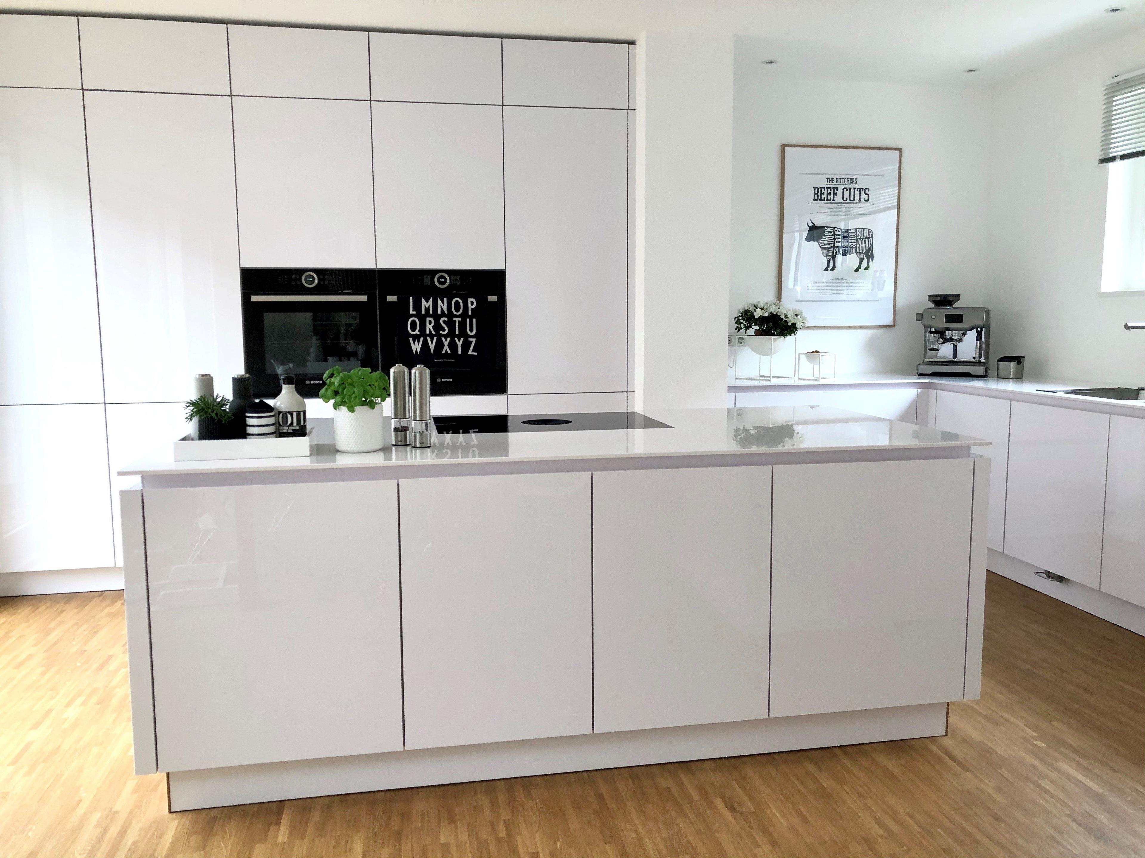 Minimalistische weiße Küche mit Kücheninsel, schwarzen Einbaugeräten, weißer Arbeitsplatte und skandinavischem Design