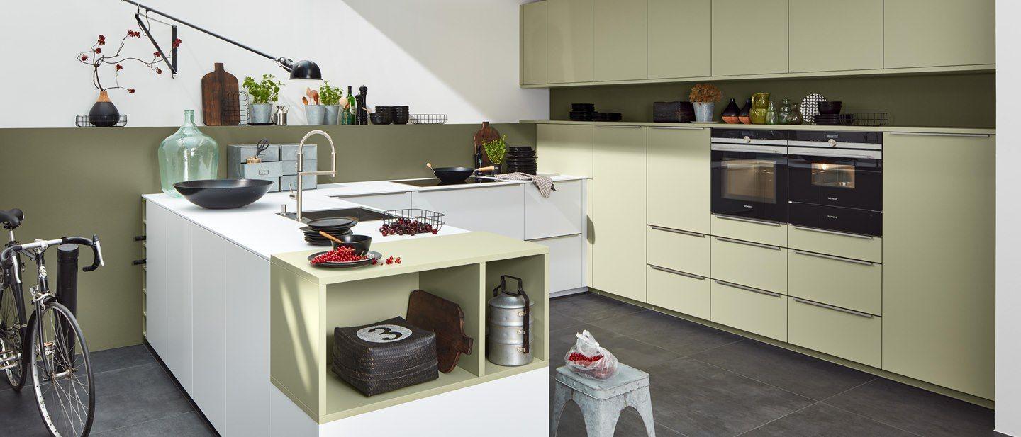 Moderne Küche mit Avocado-Farben, weißen Fronten und stilvollem Design, ergänzt durch Pflanzen und dekorative Accessoires.