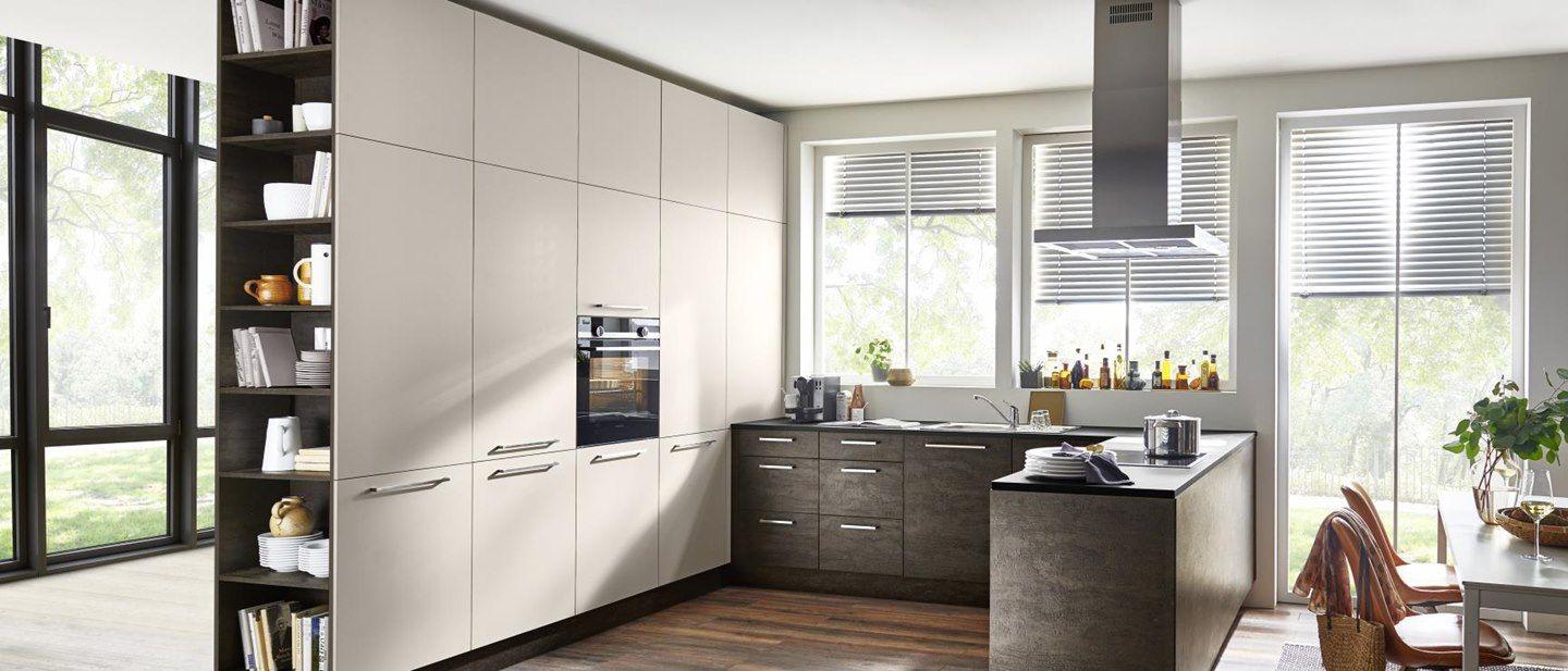 Moderne Küche mit hellen, matten Fronten und dunklem Holztisch, ergänzt durch offene Regale mit Geschirr und Kochutensilien sowie großen Fenstern, die viel Tageslicht hereinlassen.