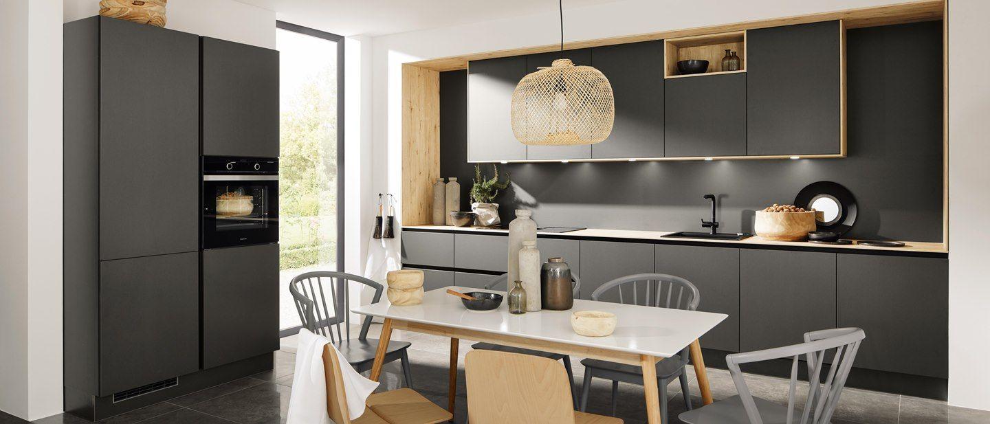 Elegante, minimalistische Küche in Schwarz und Holzoptik, ergänzt durch einen Essbereich mit skandinavischen Stühlen und natürlichen Akzenten. Große Fenster lassen viel Licht herein.