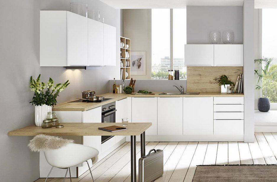 Helle, minimalistische Küche mit weißen Fronten und Holzregalen, einer Spüle und einem Kochbereich. Der Raum ist großzügig mit viel Tageslicht und modernen Möbeln wie einem Stuhl und einer Liege ausgestattet.