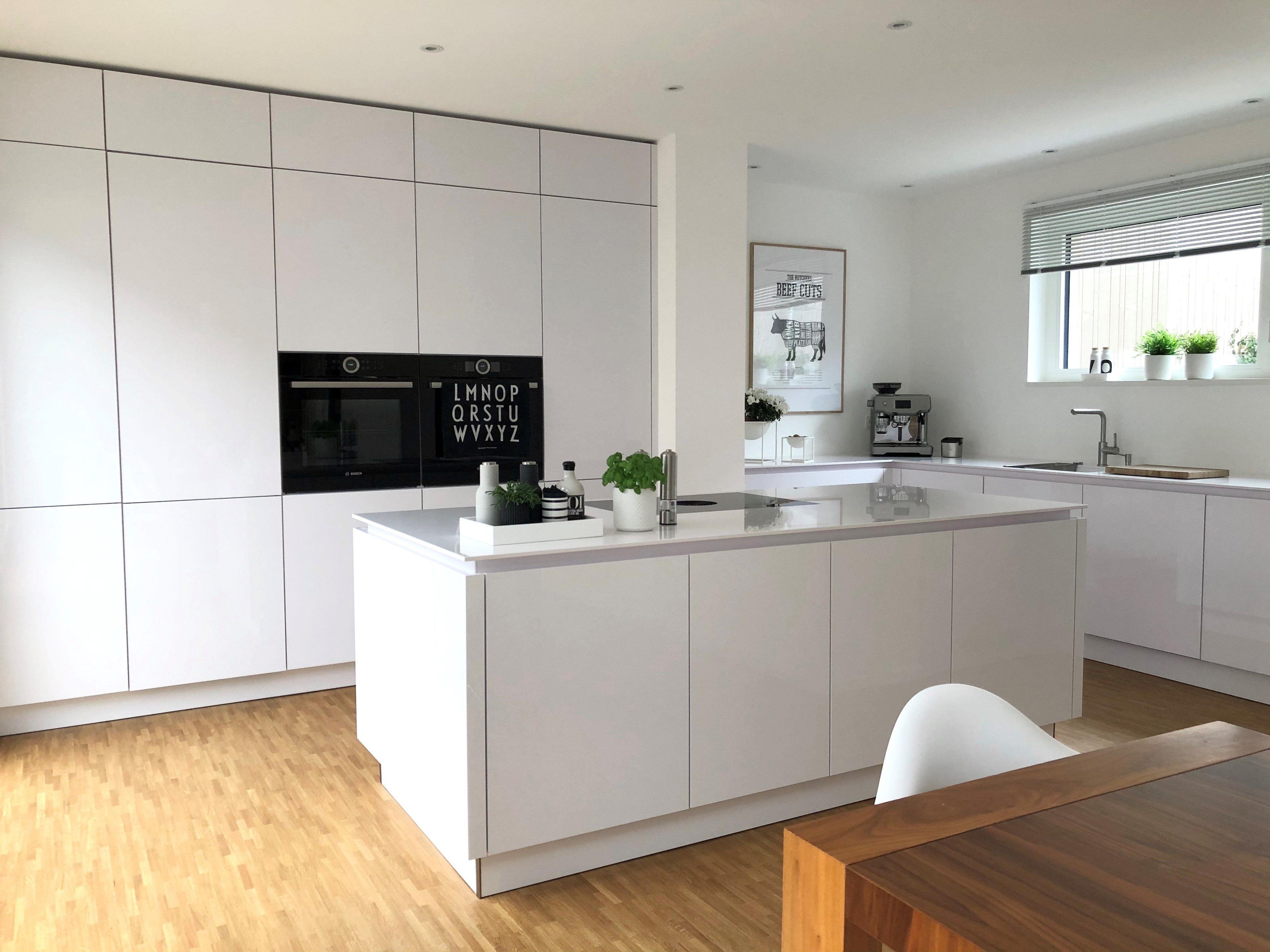 Offene Küche mit weißer Kücheninsel, eingebauten Elektrogeräten, Holzesstisch und modernem Wohndesign