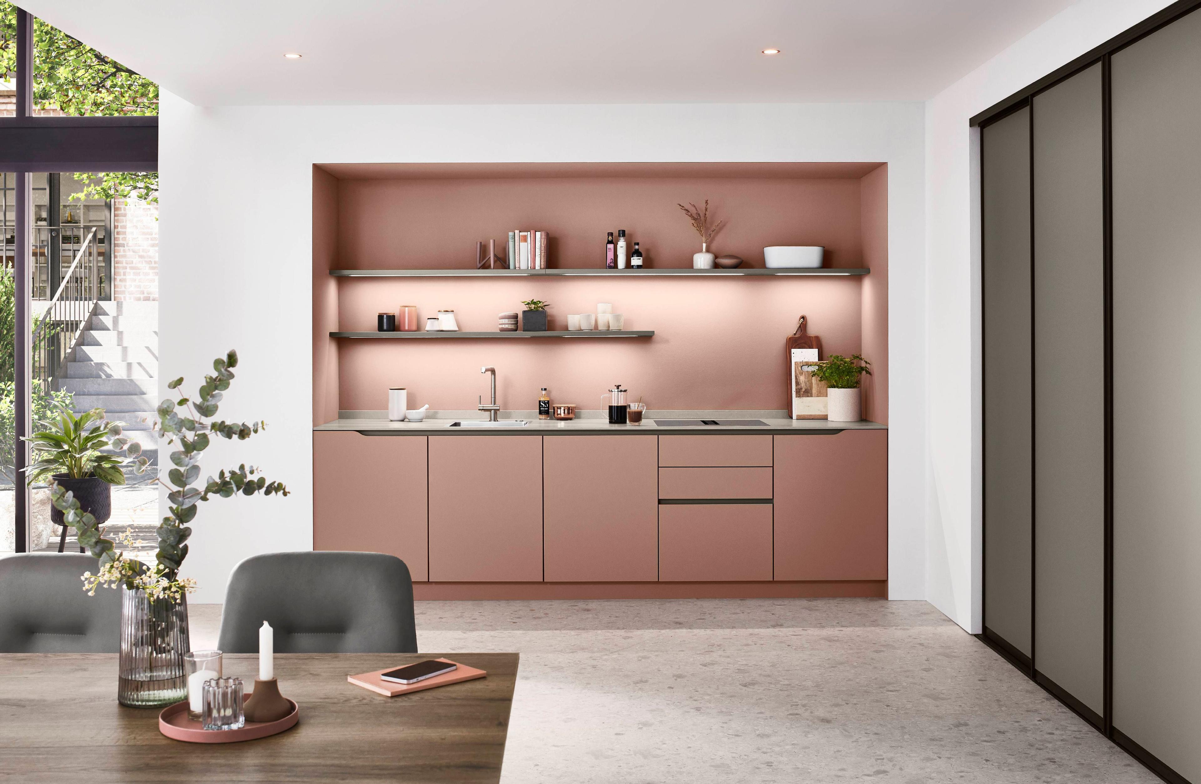 Moderne Küche in zartem Rosé mit offenen Regalen und funktionalen Geräten. Die Wand hinter der Spüle ist dezent beleuchtet und bietet Platz für dekorative Accessoires.