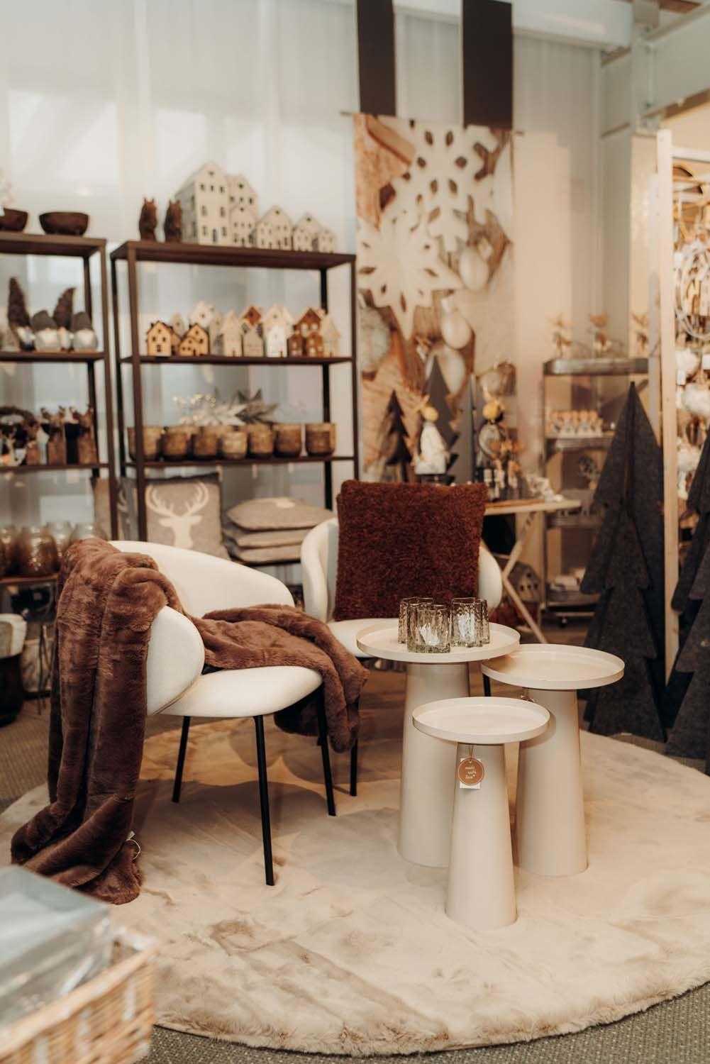 Stilvolle Sitzecke in der Boutique mit weißem Stuhl, brauner Strickdecke und weihnachtlicher Deko-Präsentation.