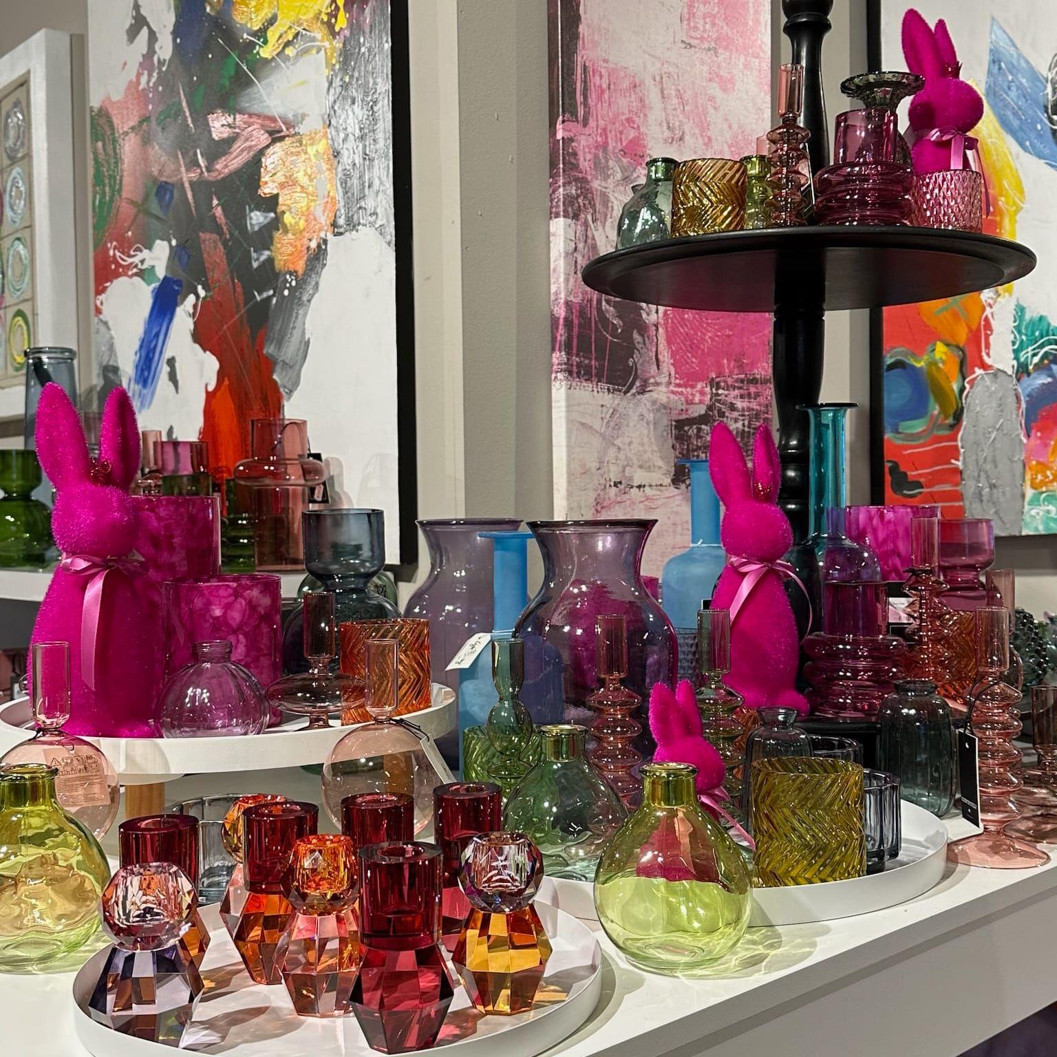 Nahaufnahme: Bunte Glasvasen in Pink, Grün und Blau mit pinken Osterhasen vor abstrakten Kunstwerken.