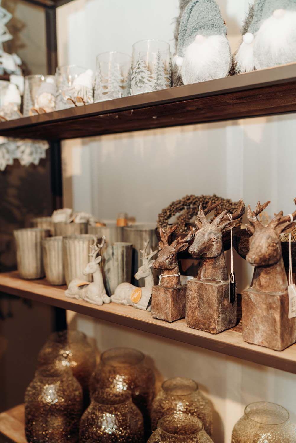 Boutique-Regal mit rustikalen Hirschfiguren aus Holz, goldenen Windlichtern und winterlicher Deko in Braun-Gold-Tönen.
