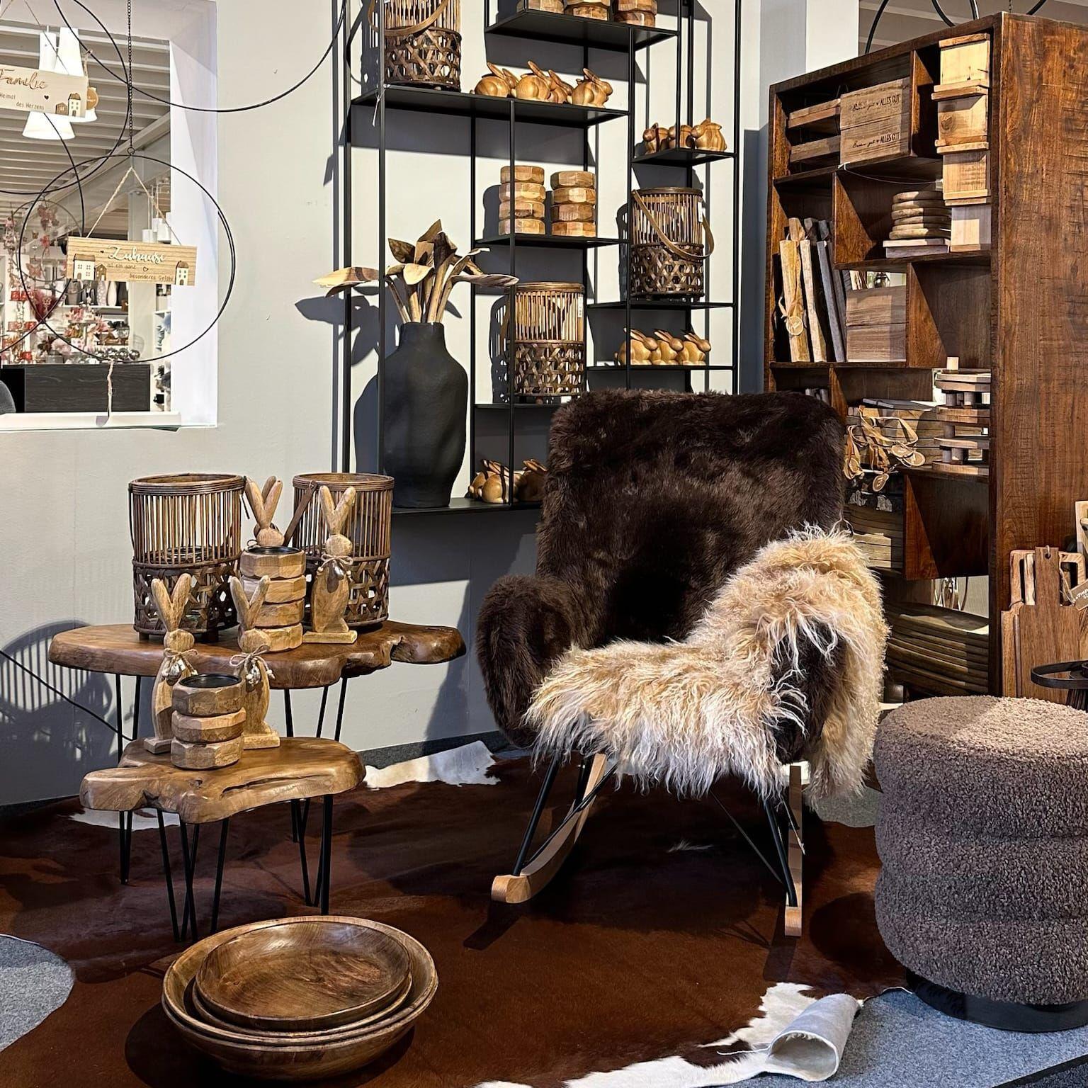 Gemütlicher Schaukelstuhl mit Fell vor schwarzem Regal voller Holzaccessoires und natürlicher Deko-Elemente.