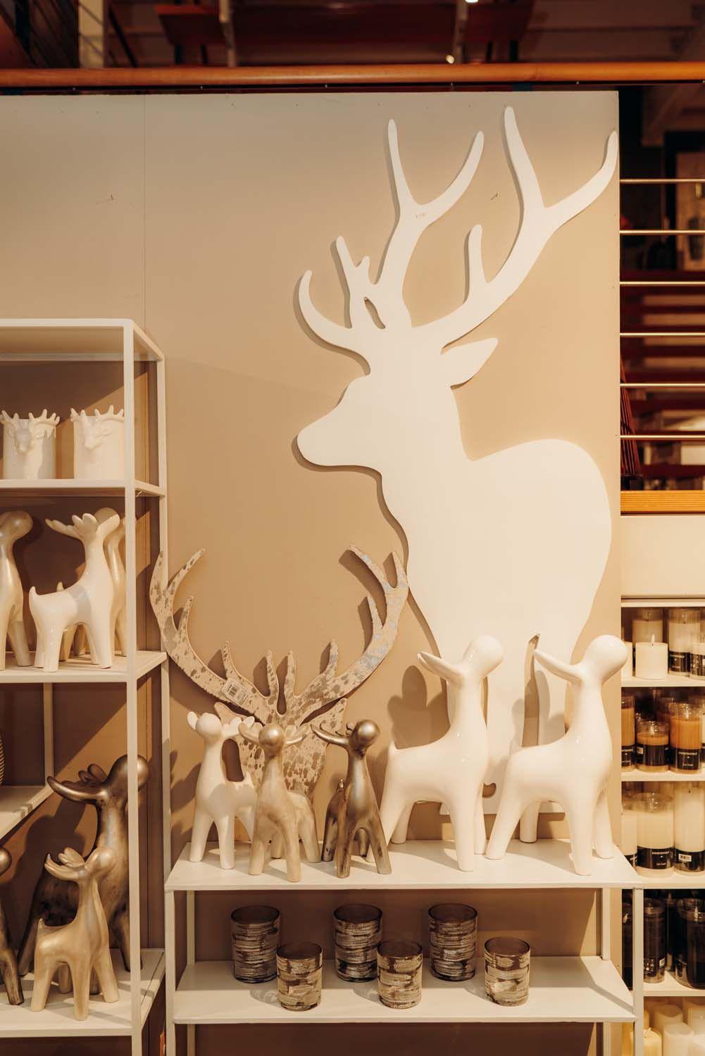 Große weiße Hirsch-Silhouette an der Wand mit verschiedenen Hirschfiguren und Windlichtern als moderne Winterdeko-Präsentation.