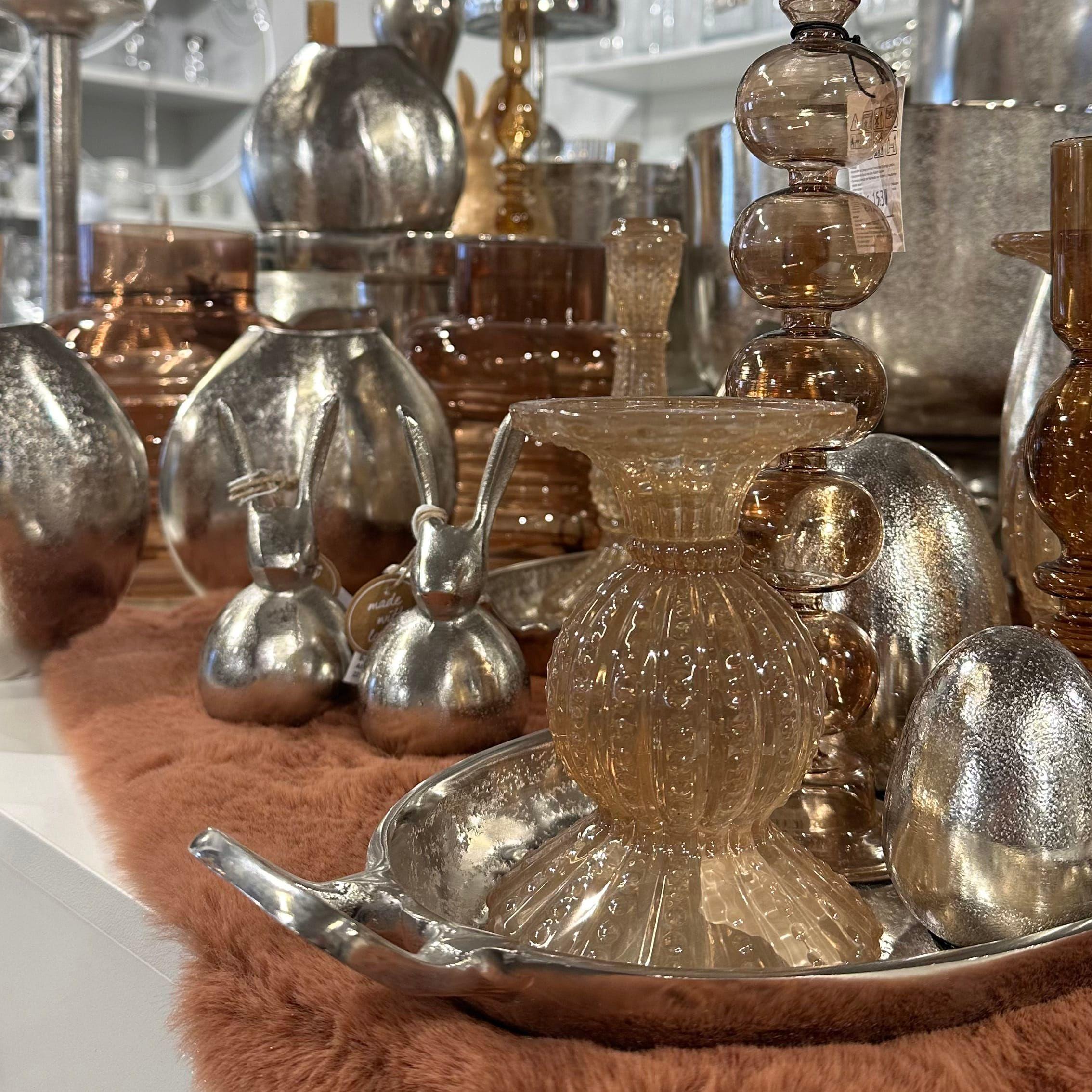 Elegante Glasdeko-Kollektion in Brauntönen mit organischen Formen auf warmer Holzoberfläche bei Möbel Grell.