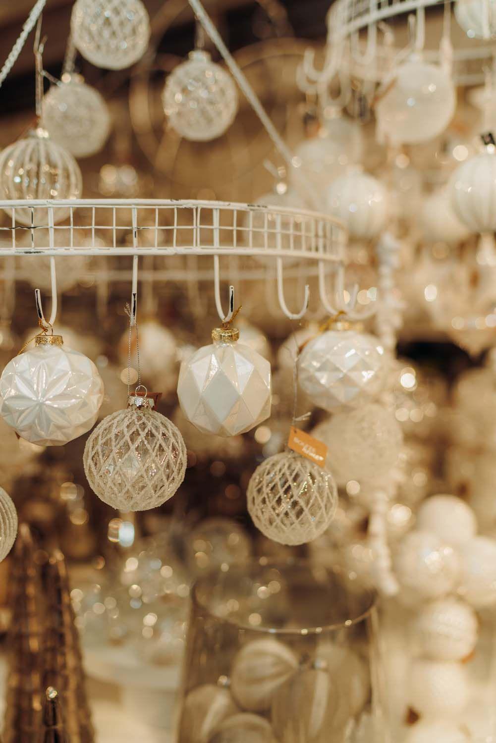  Edle Christbaumkugeln in Weiß und Gold mit verschiedenen Reliefmustern an weißem Metallgestell in der Boutique.