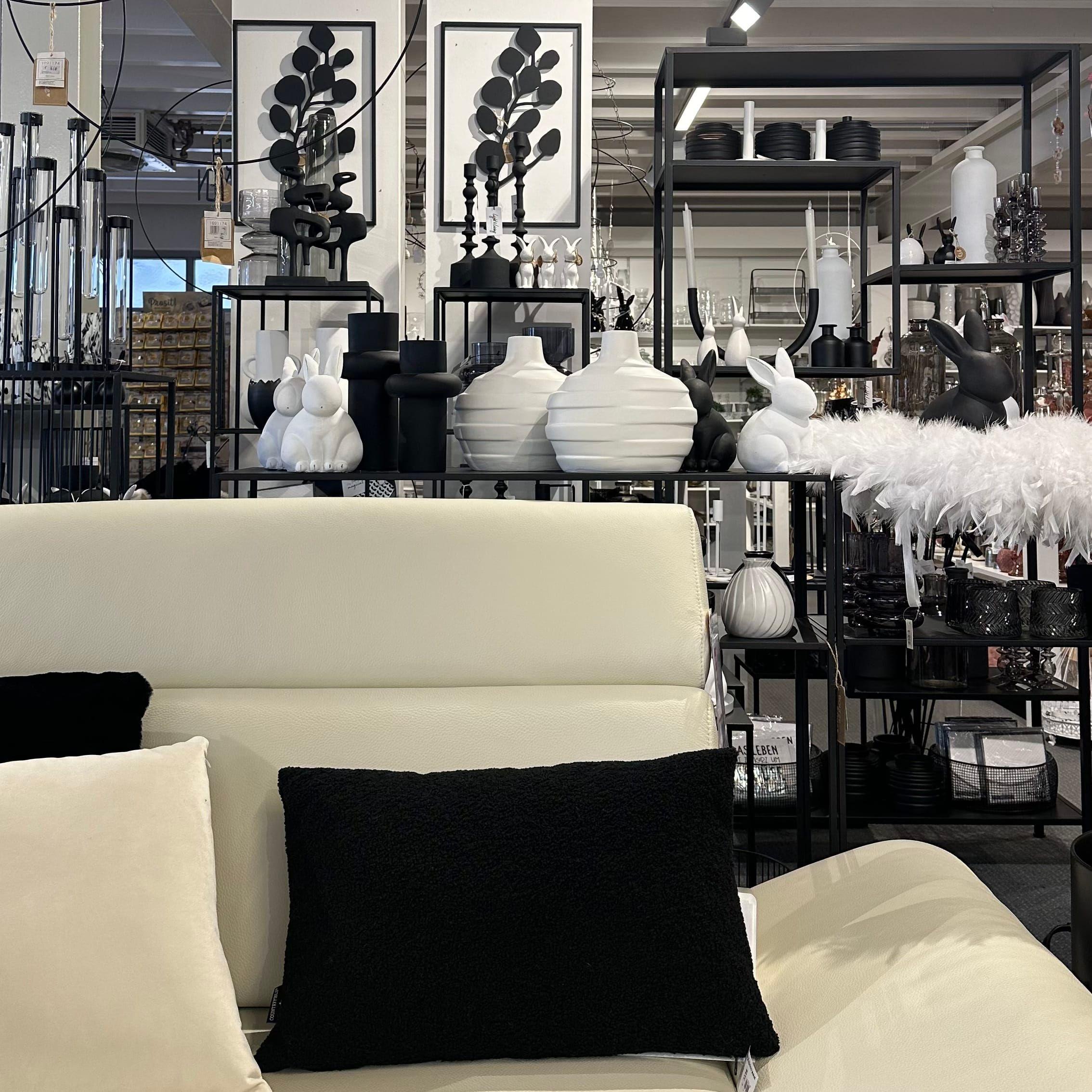 Schwarz-weiße Boutique-Präsentation mit weißen Hasen, schwarzen Vasen und modernen Wandbildern in minimalistischem Design.