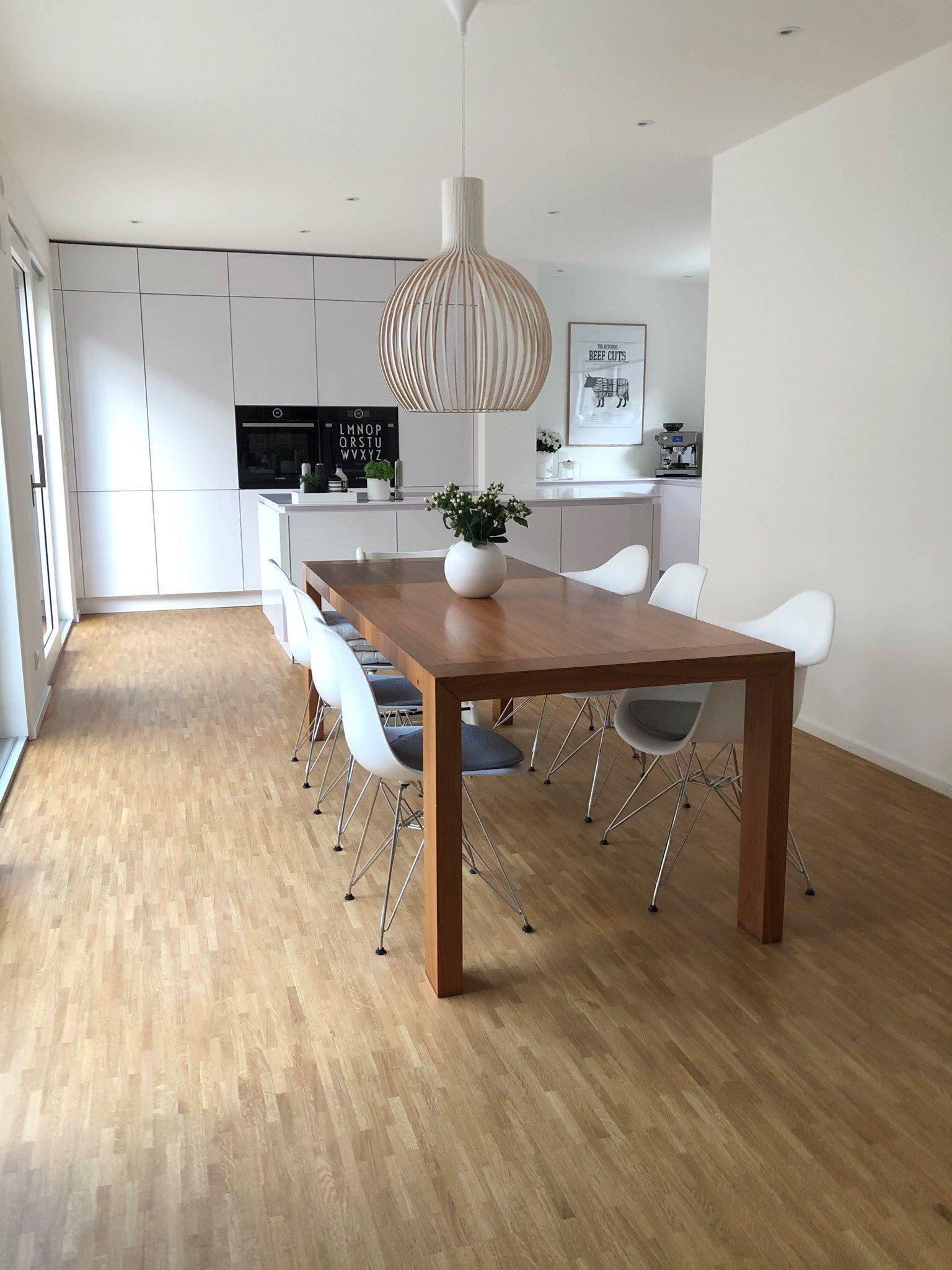 Essplatz mit Holztisch, weißen Designer-Stühlen, moderner Pendelleuchte und offener weißer Küche.