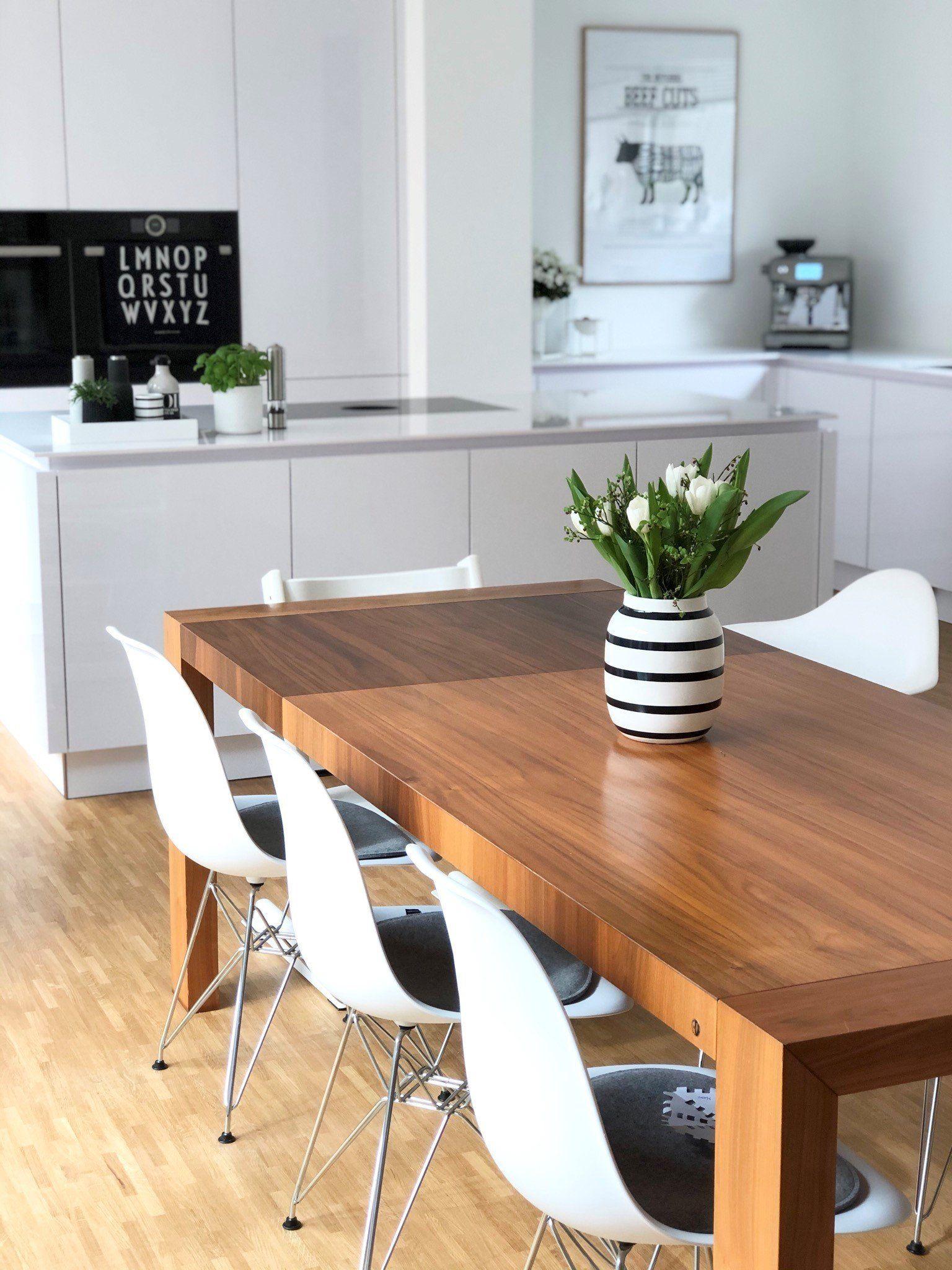 Essbereich mit Holztisch, weißen Eames-Stühlen, schwarz-weiß gestreifter Vase mit Tulpen und weißer Küche im Hintergrund,