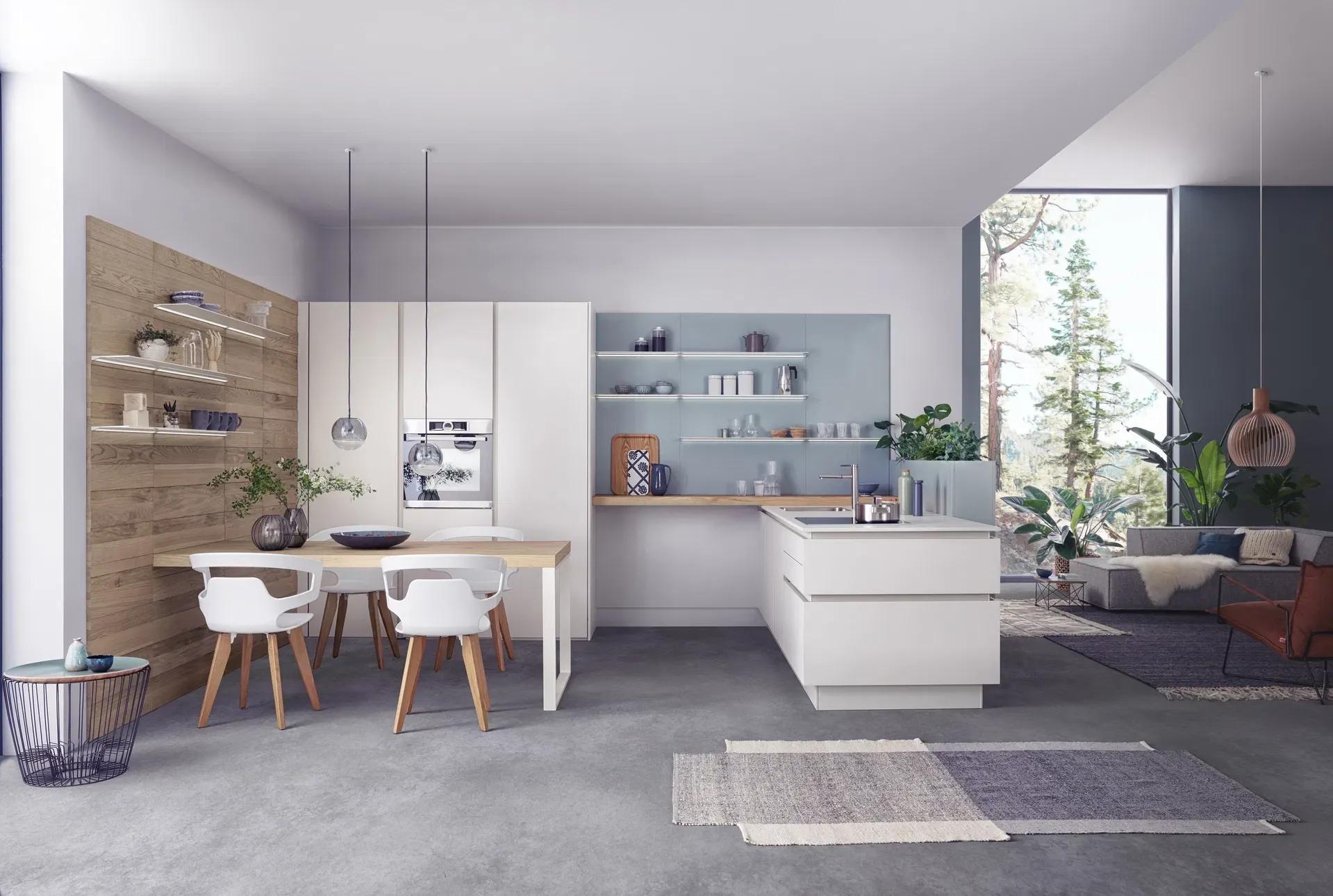 Moderne Küche in minimalistischer Gestaltung mit weißen Hochglanzfronten und einer Insel. Der Essbereich ist mit einem Holztisch und weißen Stühlen ausgestattet, während Pflanzen und eine offene Regalwand das Design ergänzen. Große Fenster lassen viel Tageslicht herein und bieten einen Blick auf die Natur.