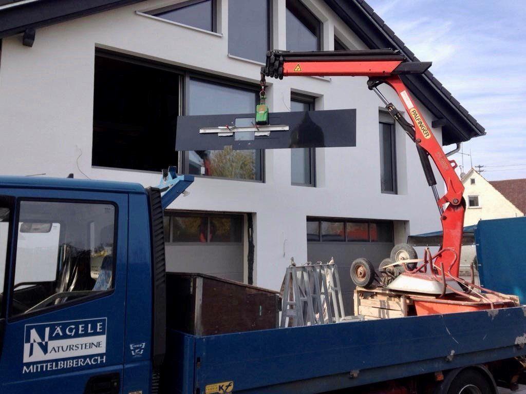 Kran-LKW hebt schwarze Treppenstufen vor modernem Neubau mit großen Fenstern