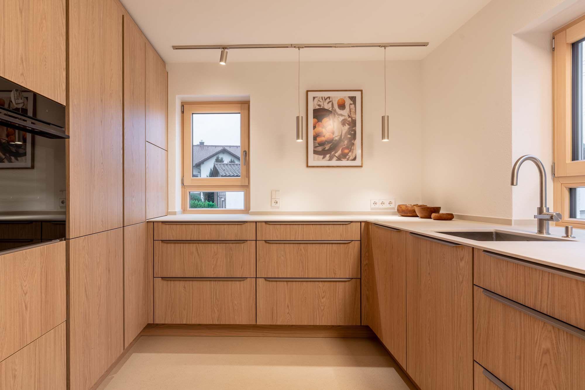 Arbeitsplatte aus hellem Mineralwerkstoff mit dekorativen Holzschalen am Fenster.
