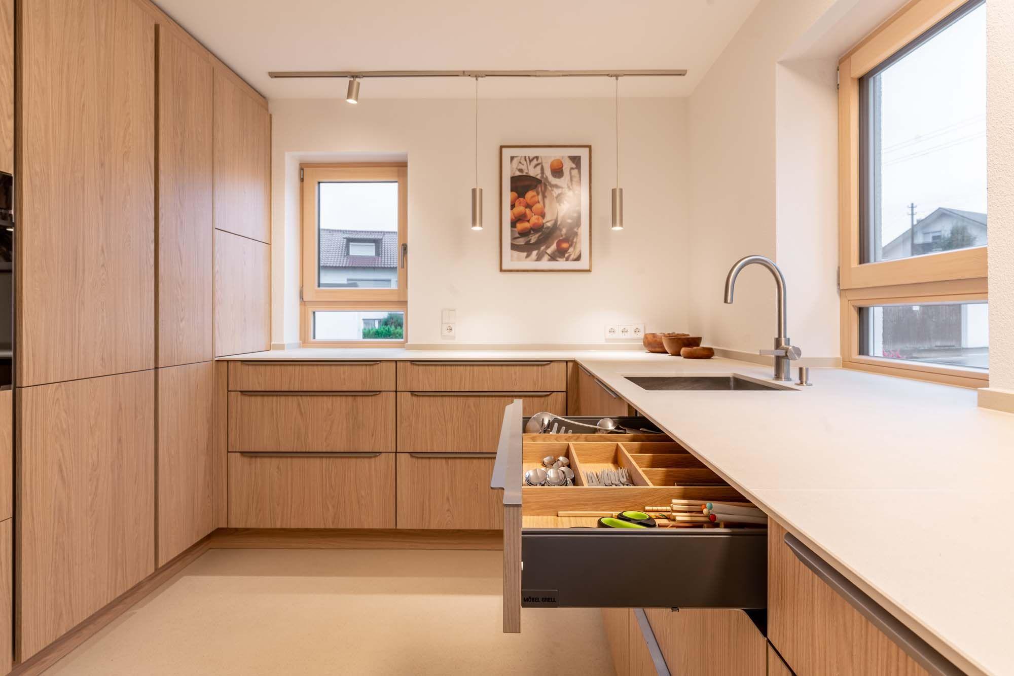 Offene Küchenschubladen mit Holz-Besteckeinsätzen und Küchenutensilien.