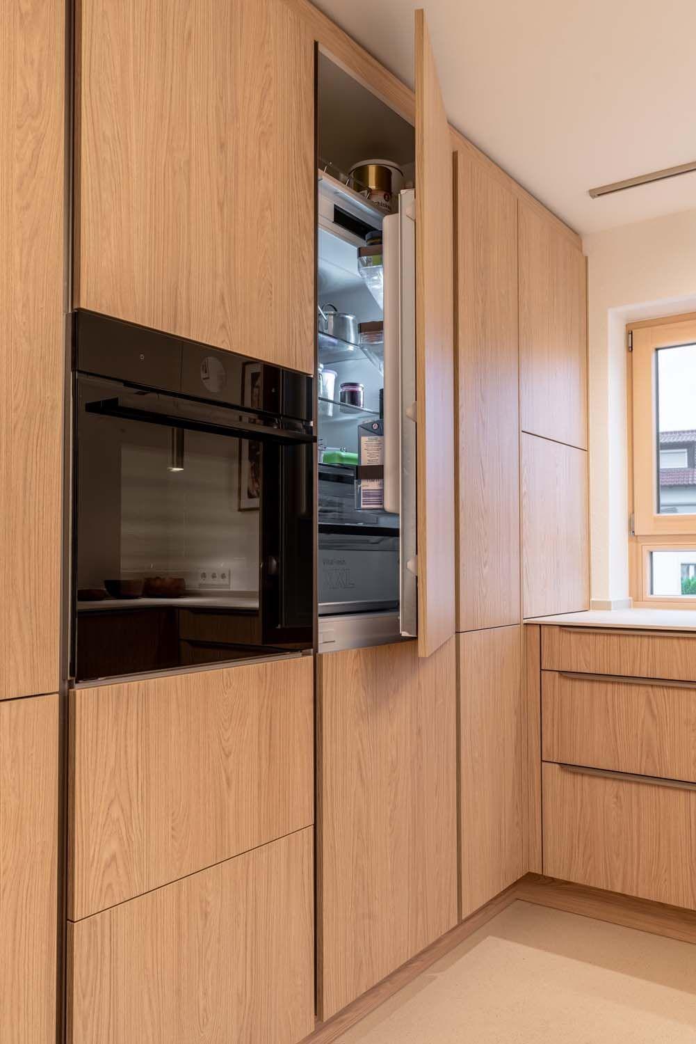 Geöffnete Hochschranktür gibt Blick auf eingebauten Kühlschrank frei.