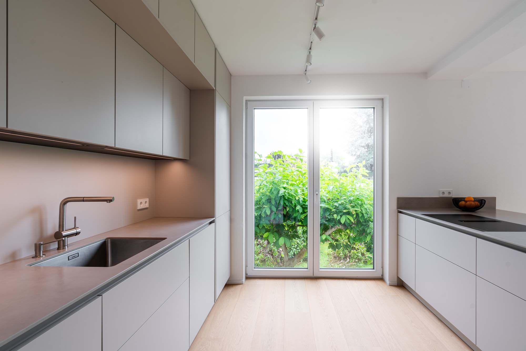 Schmale Küche mit Terrassentür, beige Oberschränken, Edelstahlspüle und hellem Eichenboden.