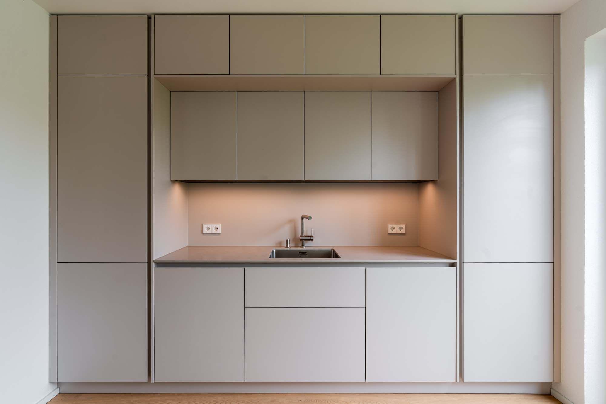 Symmetrische Küchenfront in Beige und Weiß mit zentraler Spüle, Unterschrankbeleuchtung und deckenhohen Hochschränken.