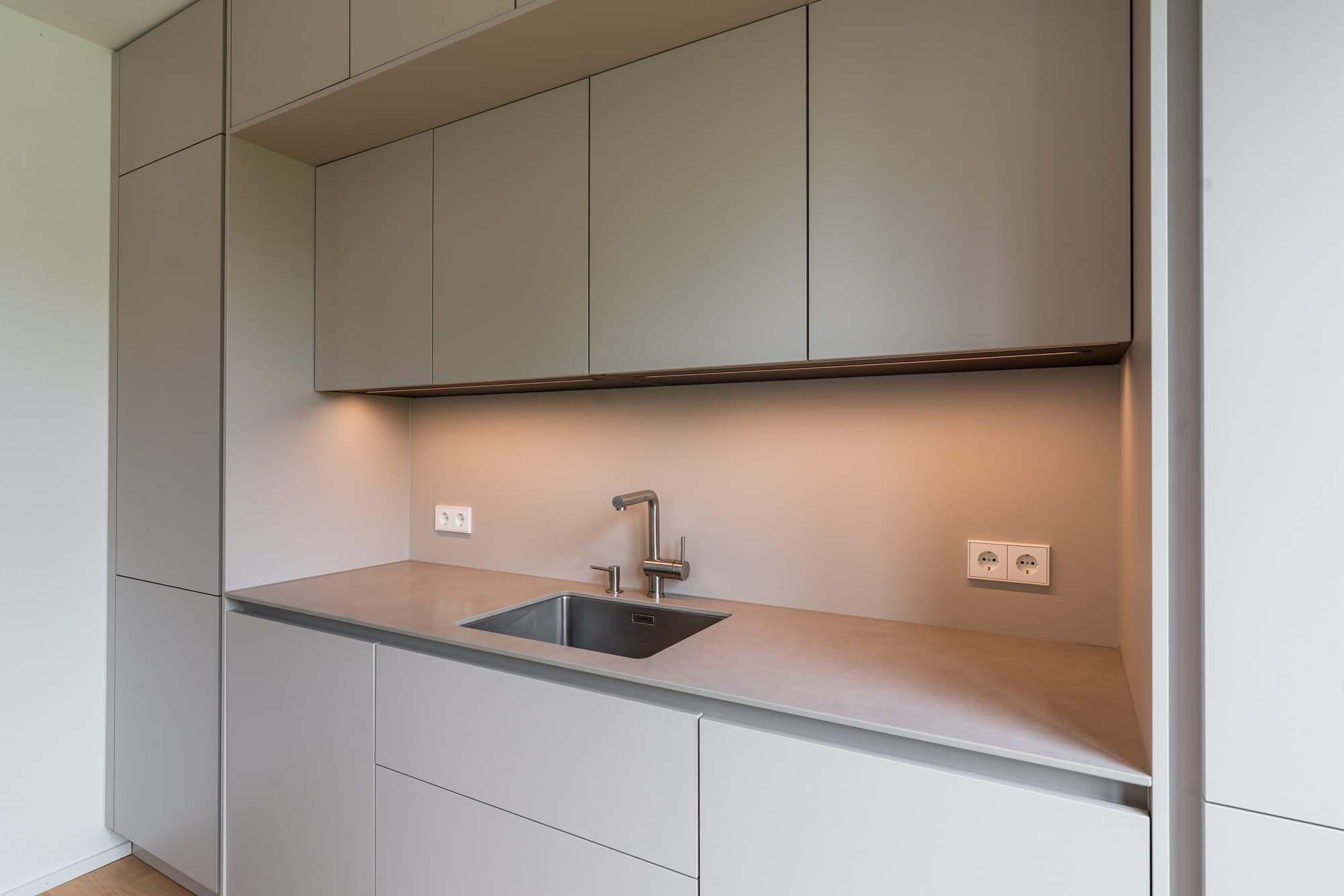 Minimalistische Küchenzeile mit beigen Oberschränken, weißen Unterschränken und warmer Arbeitsplattenbeleuchtung.
