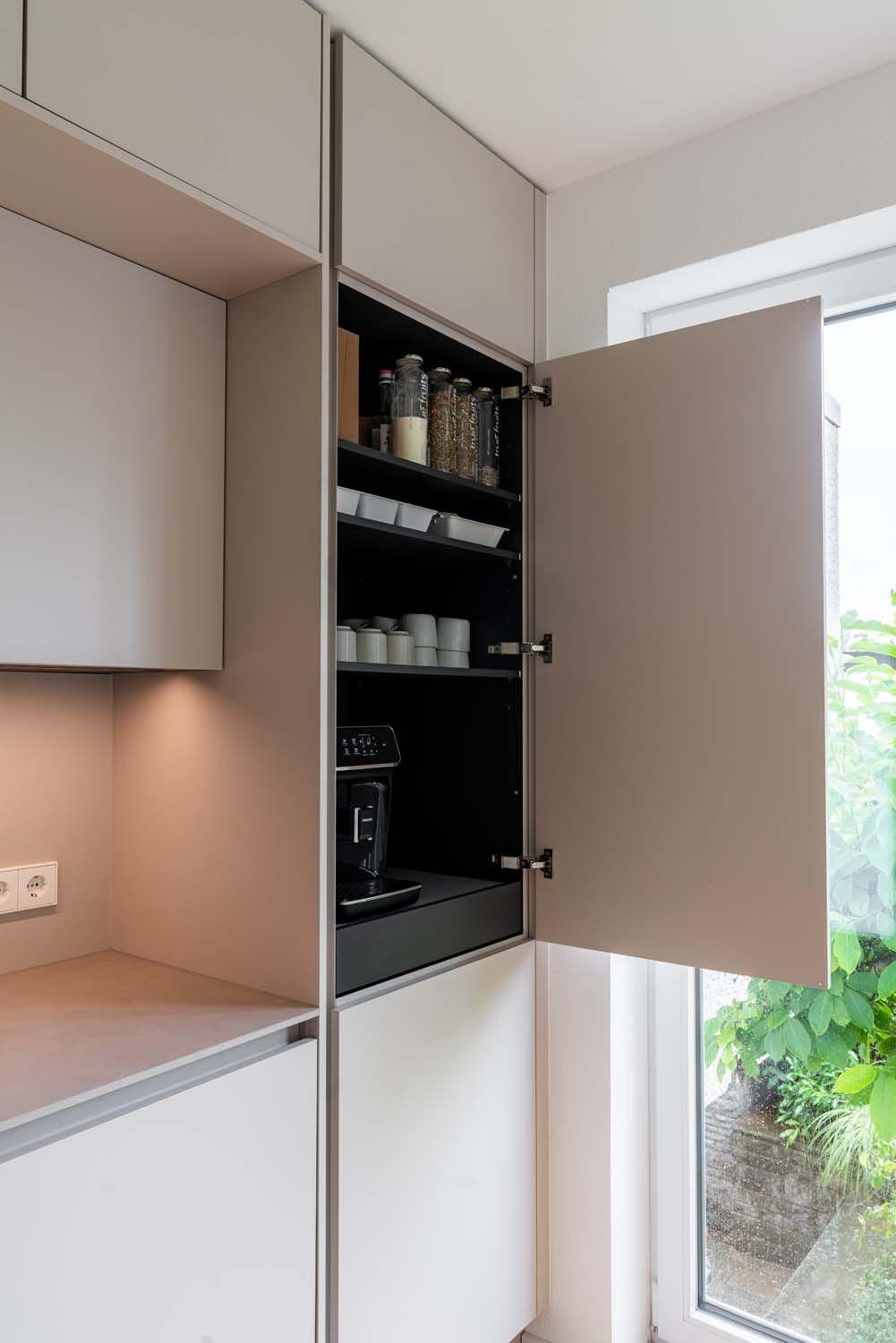 Geöffneter Hochschrank mit schwarzem Interieur, Vorratsregalen mit Gläsern und integrierter Kaffeemaschine.