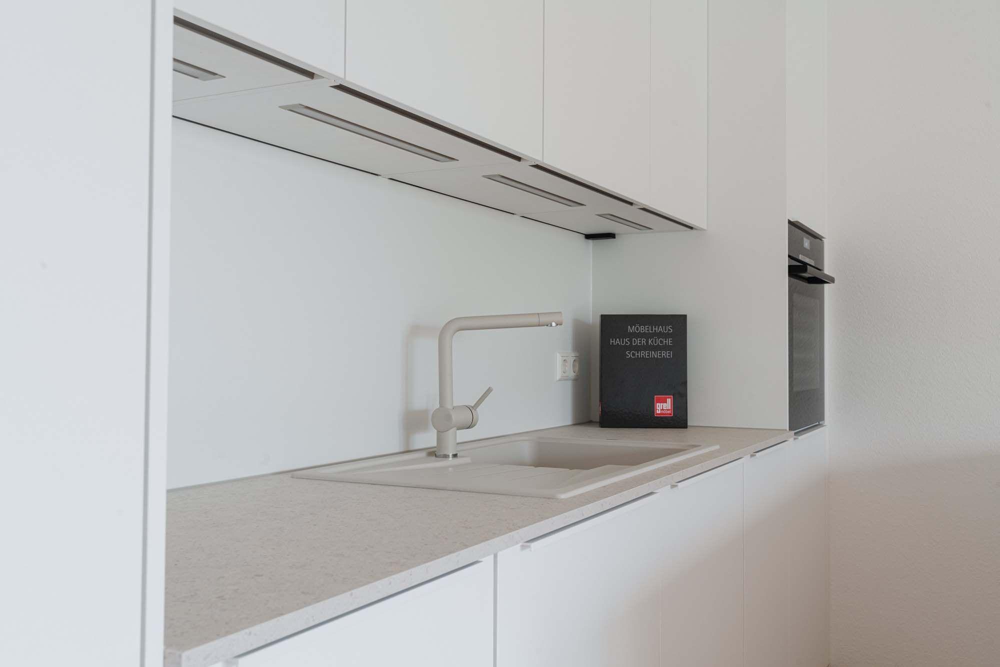 Beige Küchenarmatur an Einbauspüle mit Abtropffläche und Glasrückwand.