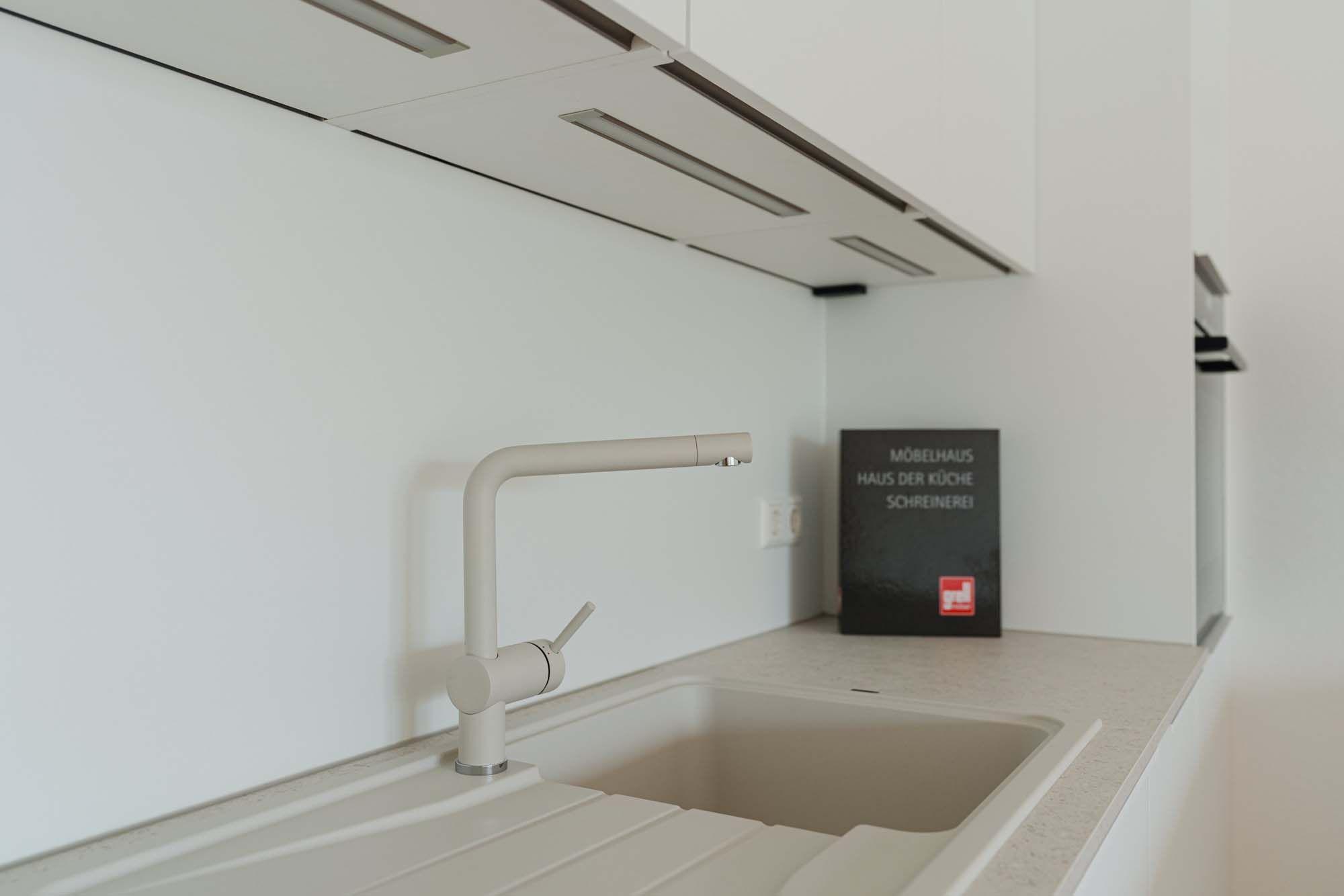 Schwenkbare Spülarmatur in Beige vor weißer Rückwand mit LED-Unterbauleuchten.