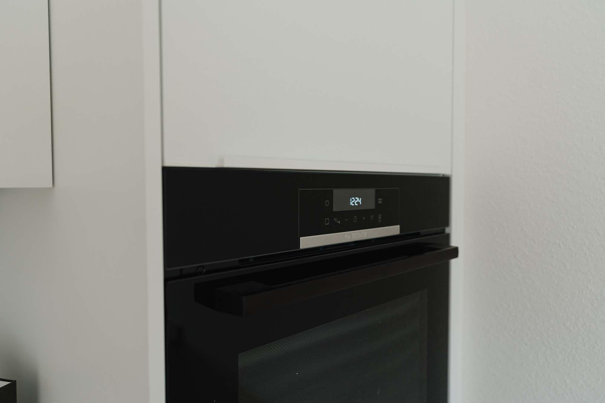 Schwarzer Einbaubackofen mit Touchdisplay und Digitalanzeige in weißer Hochschrankzeile.