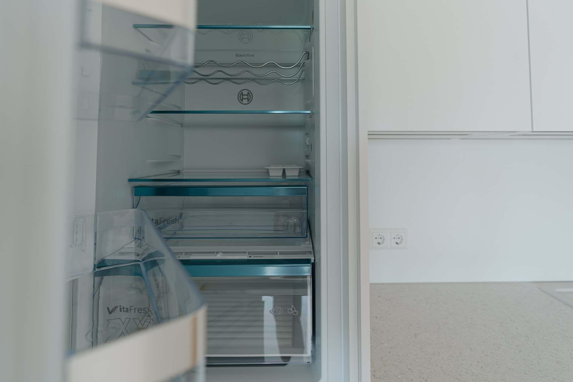 Geöffneter Einbaukühlschrank mit VitaFresh-Schubladen und Glasfachböden.