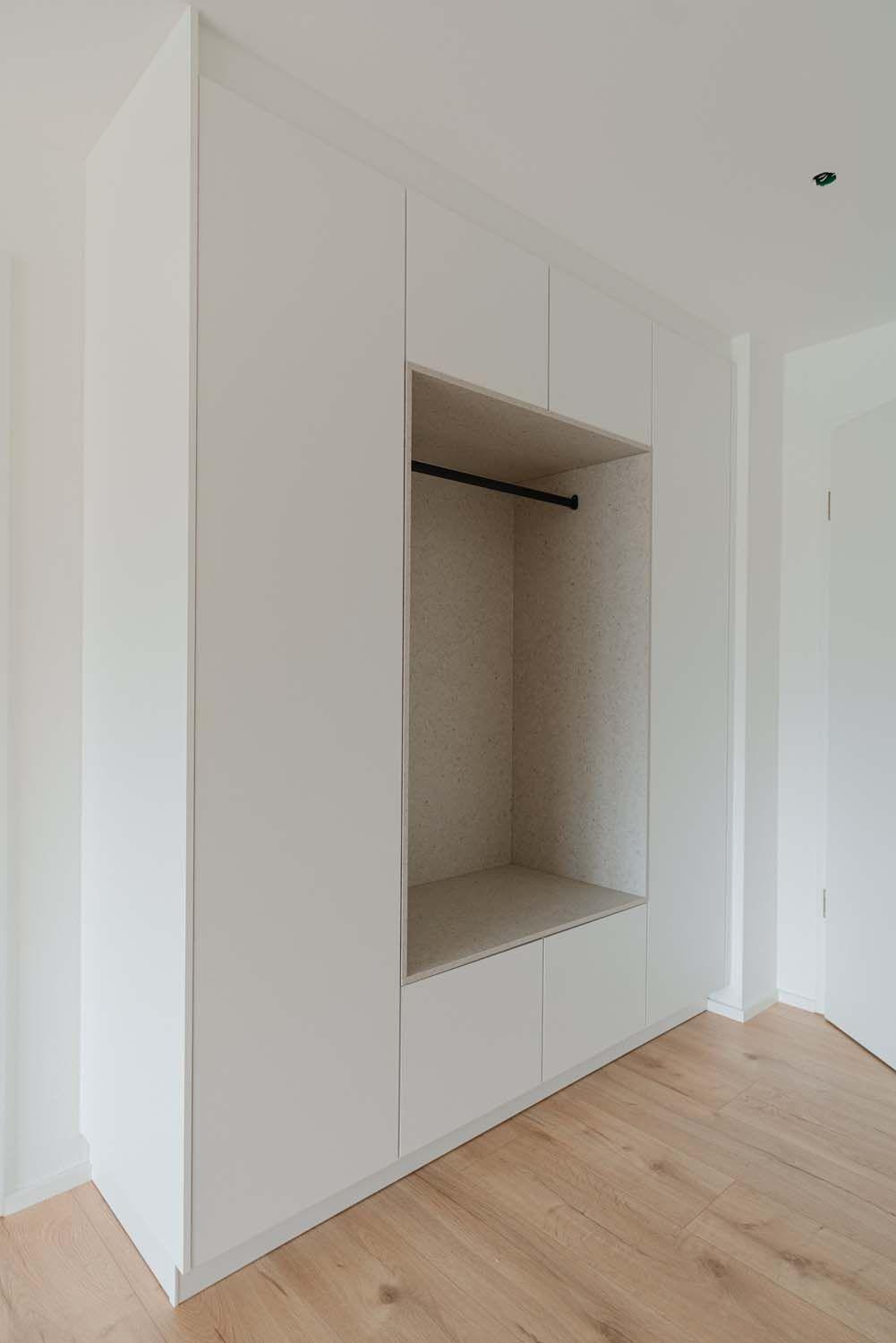 Weiße Einbaugarderobe mit offener Nische, Kleiderstange und Sitzelement.