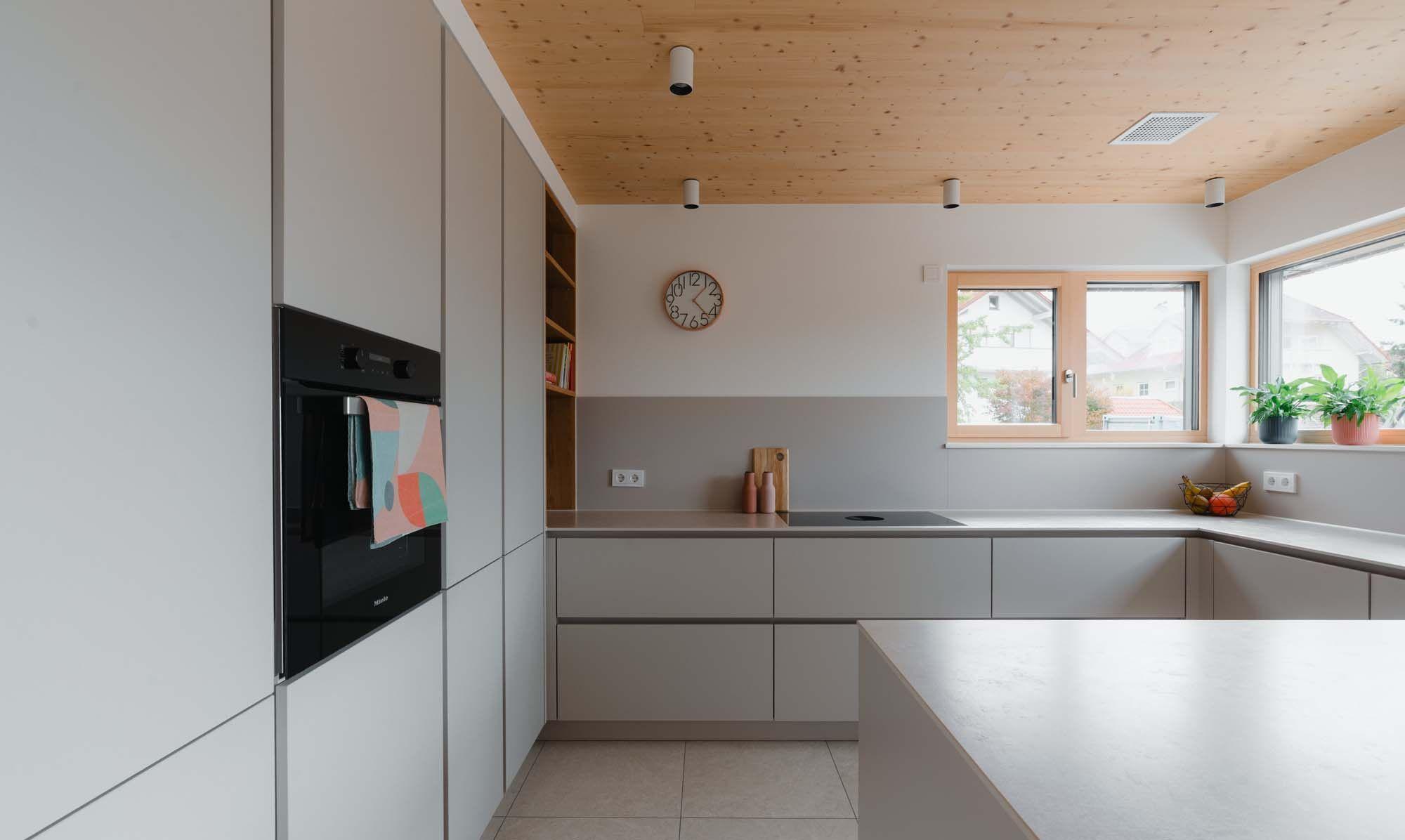 Moderne Küche mit hellgrauer U-Form, Holzdecke, großen Fenstern und integriertem Backofen in grauen Hochschrank.