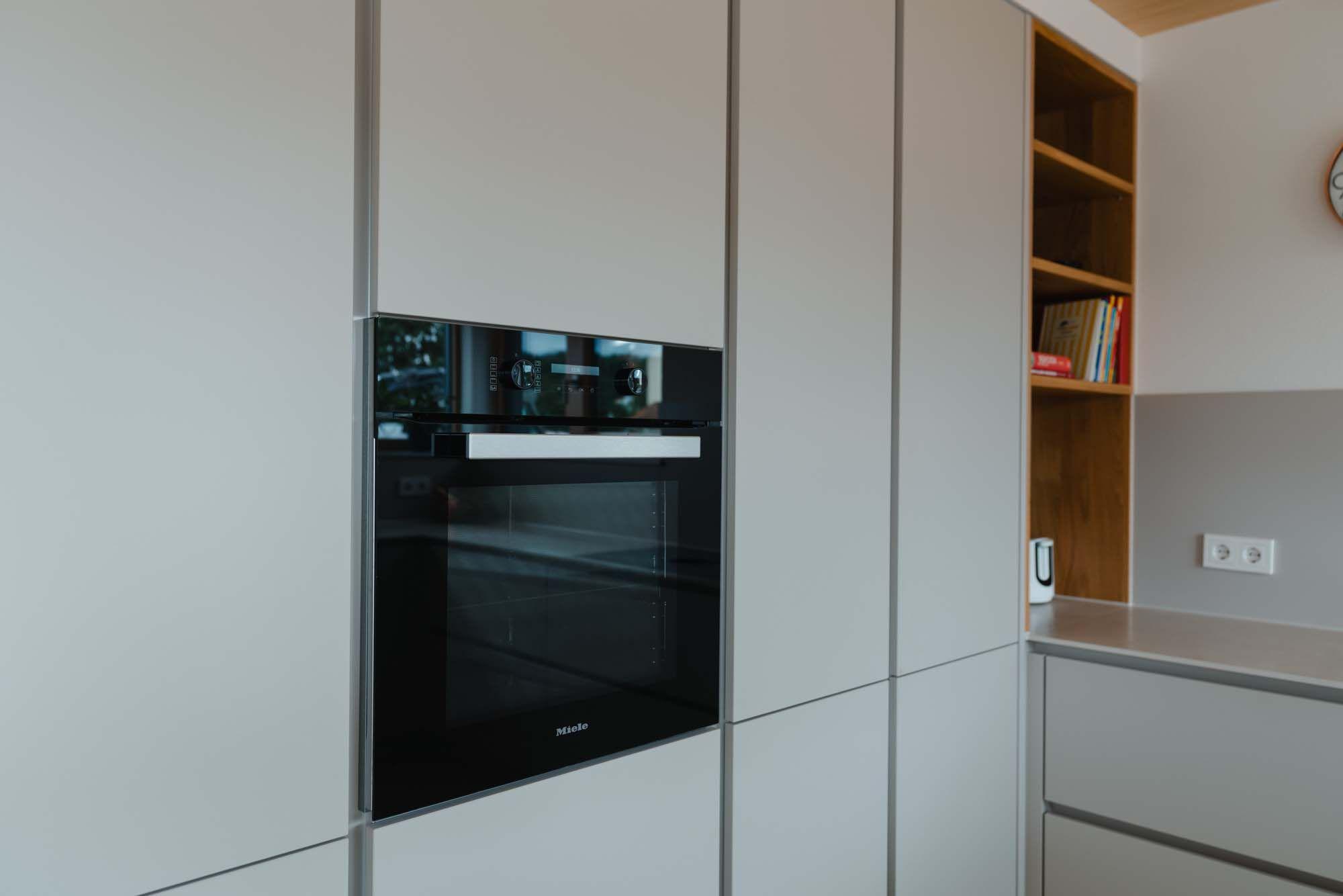 Schwarzer Einbau-Backofen in weißer griffloser Schrankfront neben Holzregal-Nische.