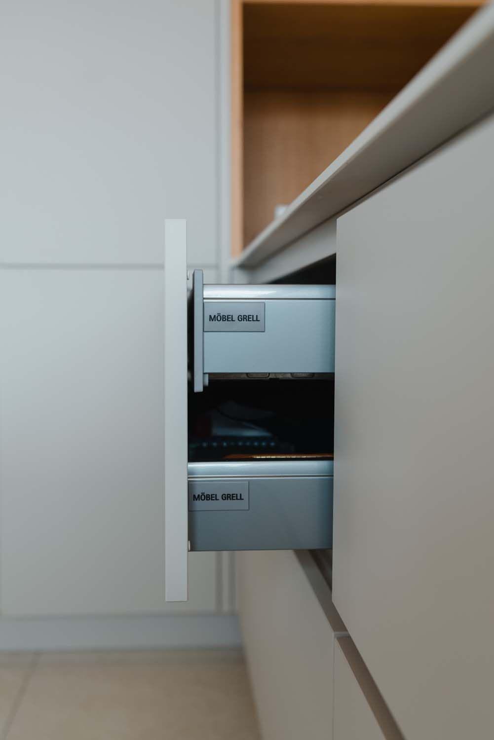 Teilweise geöffnete Küchenschublade mit "Möbel Grell"-Beschriftung und Vollauszug-System.