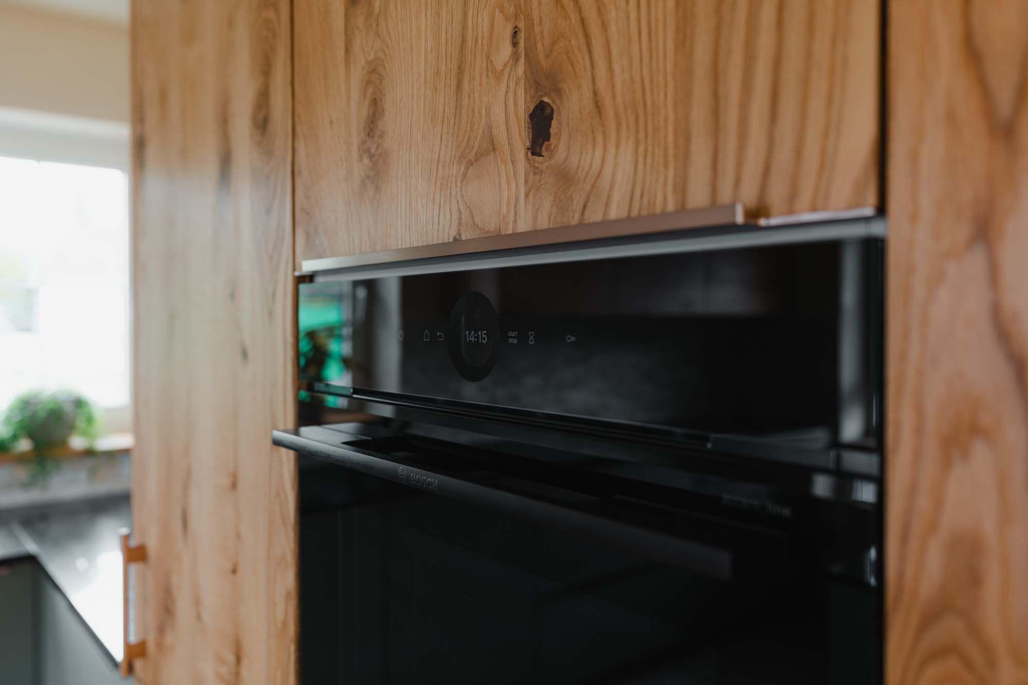 Detailansicht schwarzer Einbaubackofen mit Digitalanzeige in deckenhoher Holz-Hochschrankfront mit natürlicher Maserung.