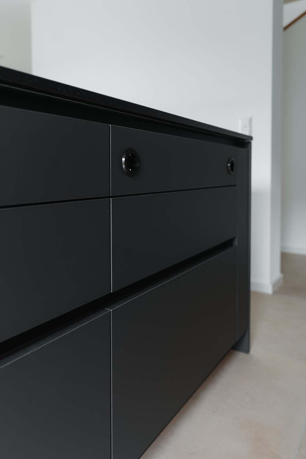 Geöffnete grifflose Schublade mit schwarzem Push-to-Open-Griff unter schwarzer Arbeitsplatte, matte dunkelgraue Front.