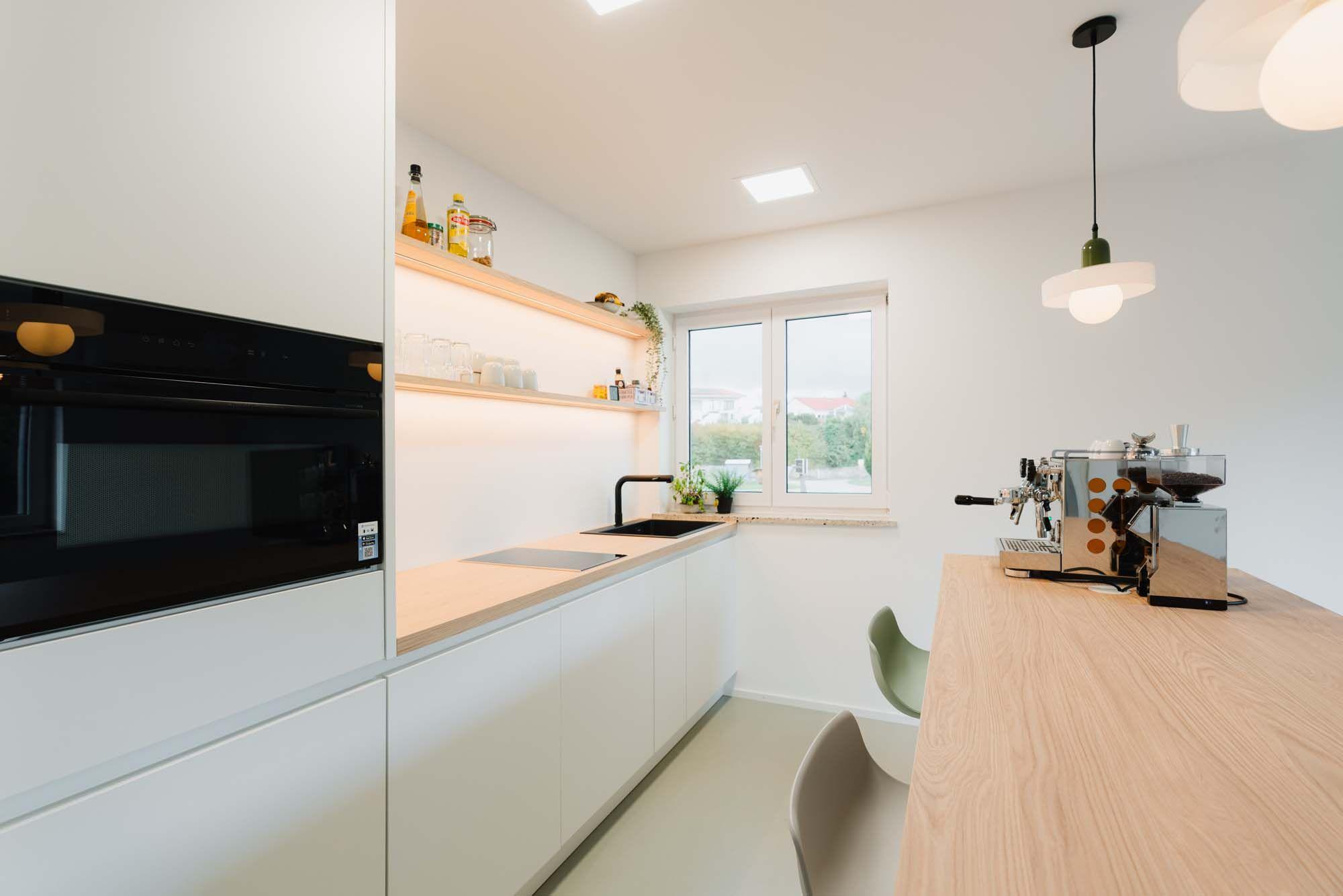 Weiße Küchenzeile mit beleuchteten Holzregalen, Espressomaschine und skandinavischem Design.