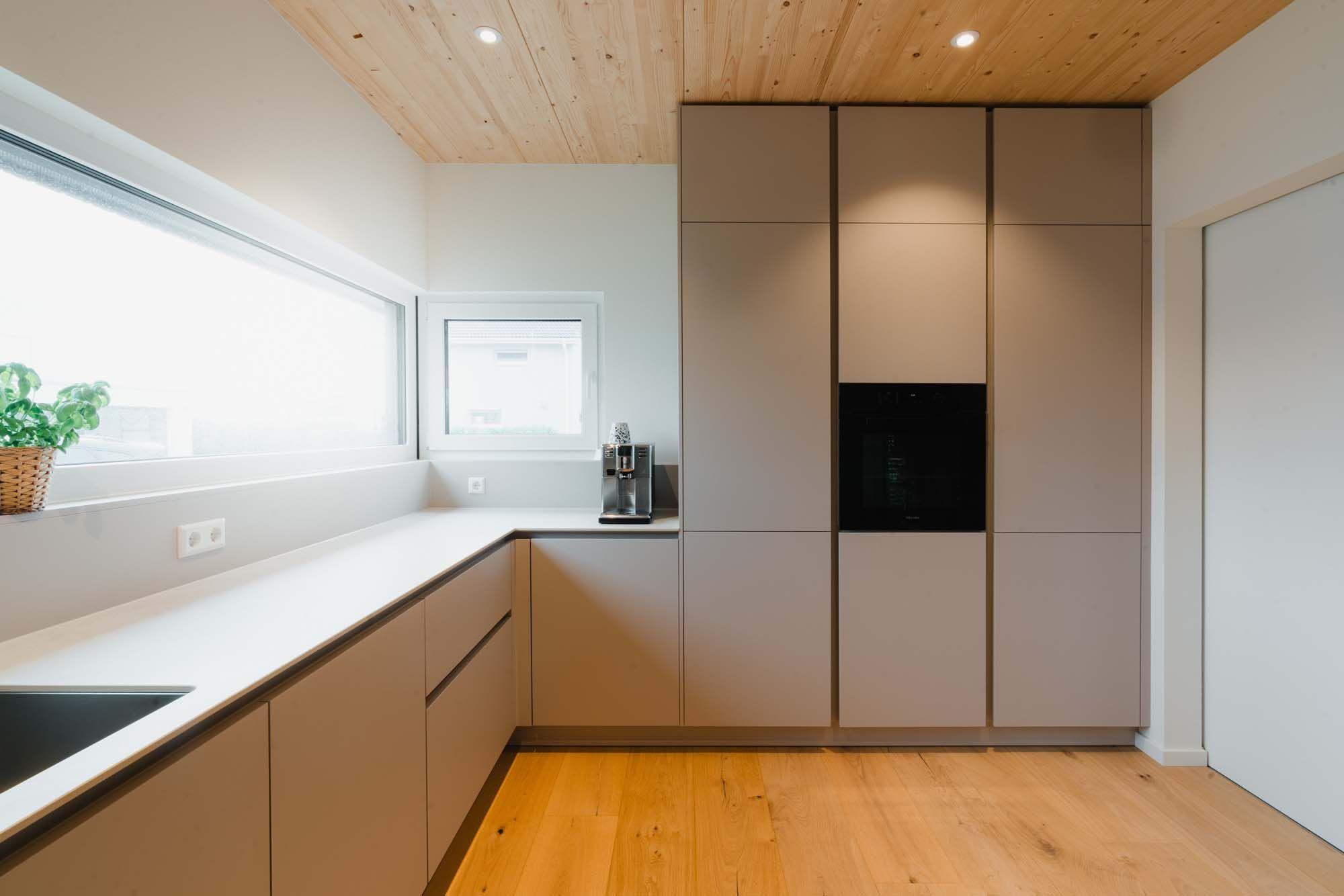 Moderne Küche mit Holzdecke, beigen grifflosen Schränken, eingebautem Backofen und hellem Holzboden.