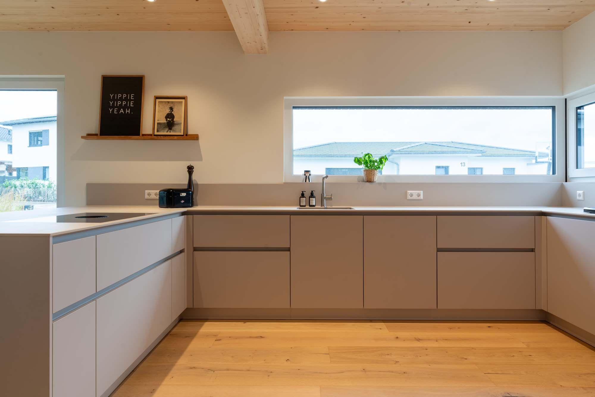 U-förmige Küche mit horizontalem Panoramafenster, beigen und weißen Fronten sowie Naturholzboden