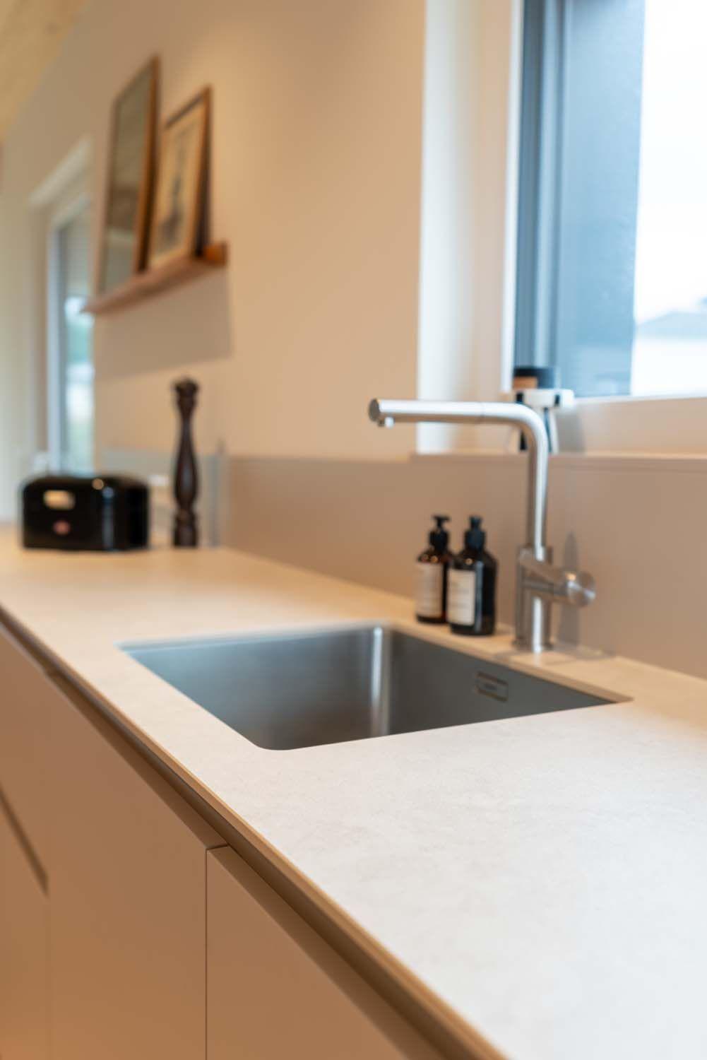Nahaufnahme einer Unterbauspüle mit modernem Chrom-Wasserhahn und Seifenspendern.