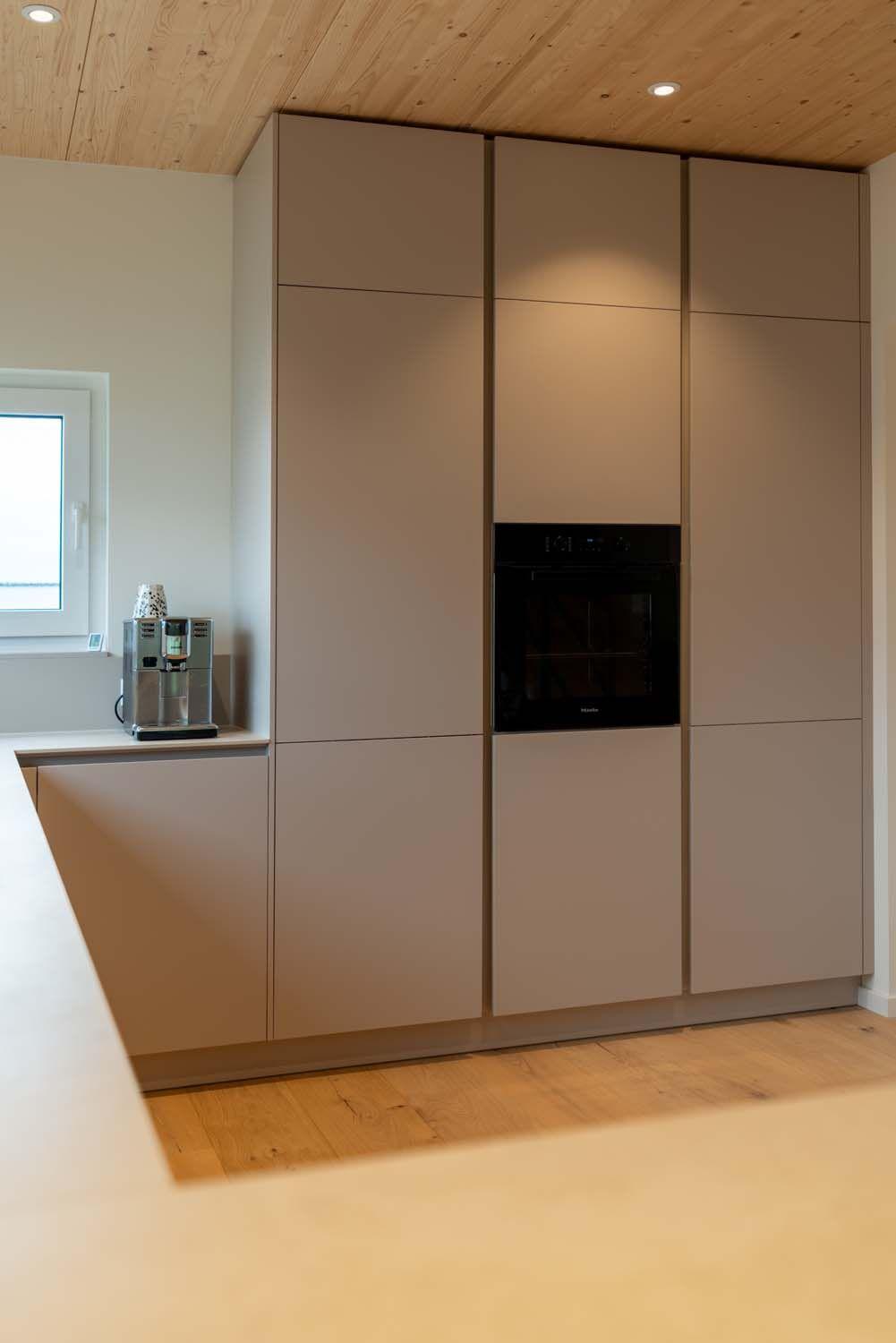 Hochschrank mit beigen grifflosen Fronten und mittig integriertem schwarzem Backofen.