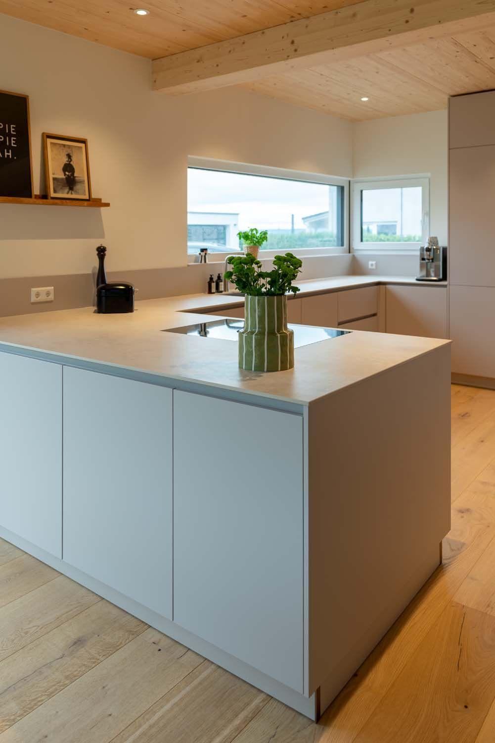 Kücheninsel mit dekorativer grüner Vase, im Hintergrund helle Fensterfront und Holzdecke.