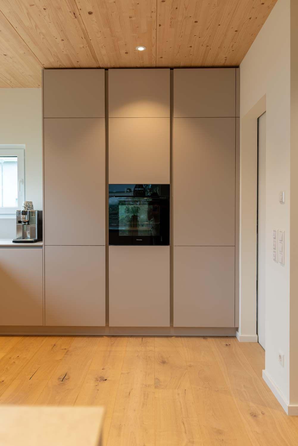 Hochschrankwand in Beige mit eingebautem Backofen unter natürlicher Holzdecke.