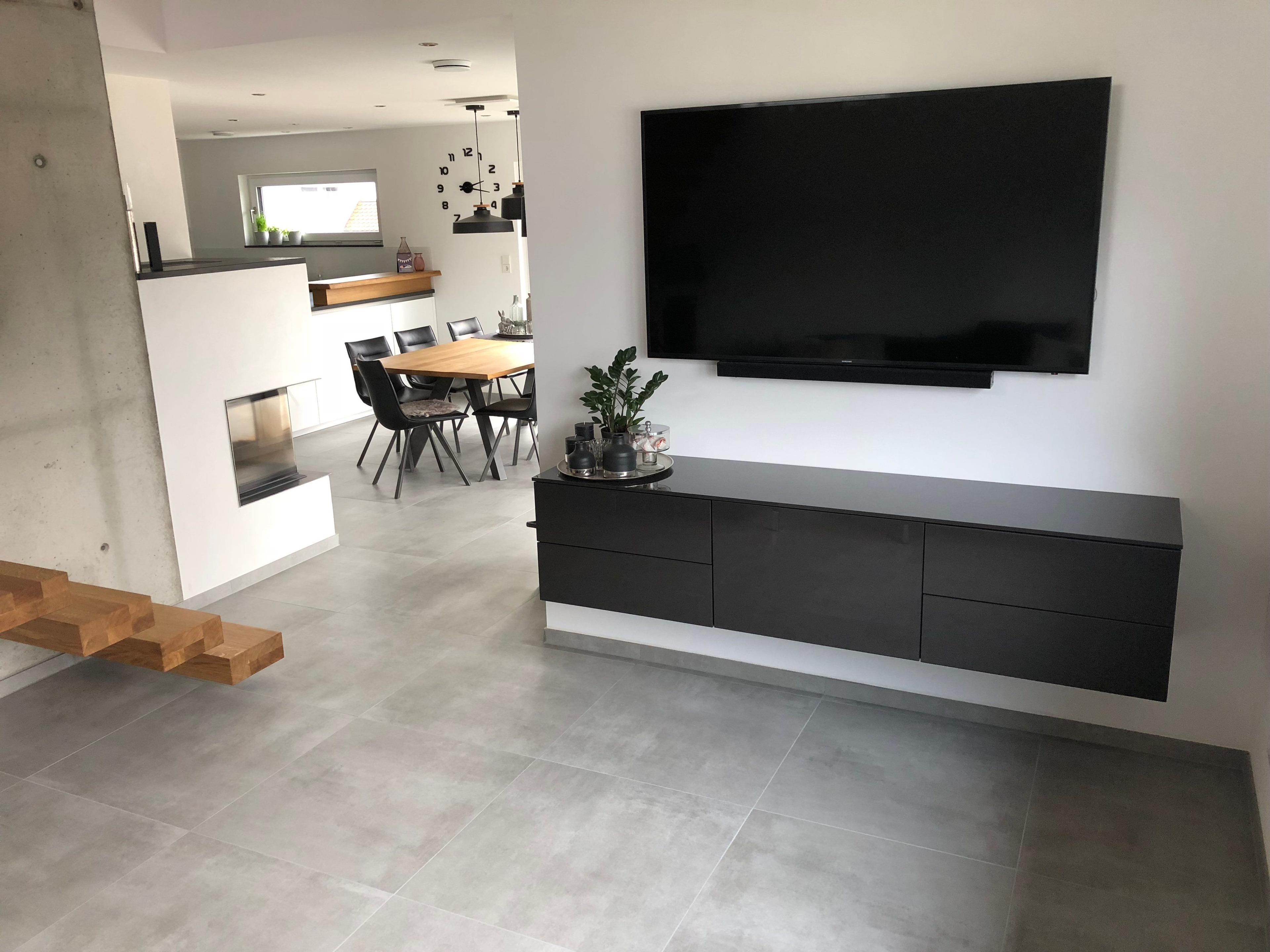 Wohnbereich mit wandmontiertem Großbild-TV, schwarzem schwebendem Sideboard, modernem Kamin und Blick in den Essbereich mit Holztisch.
